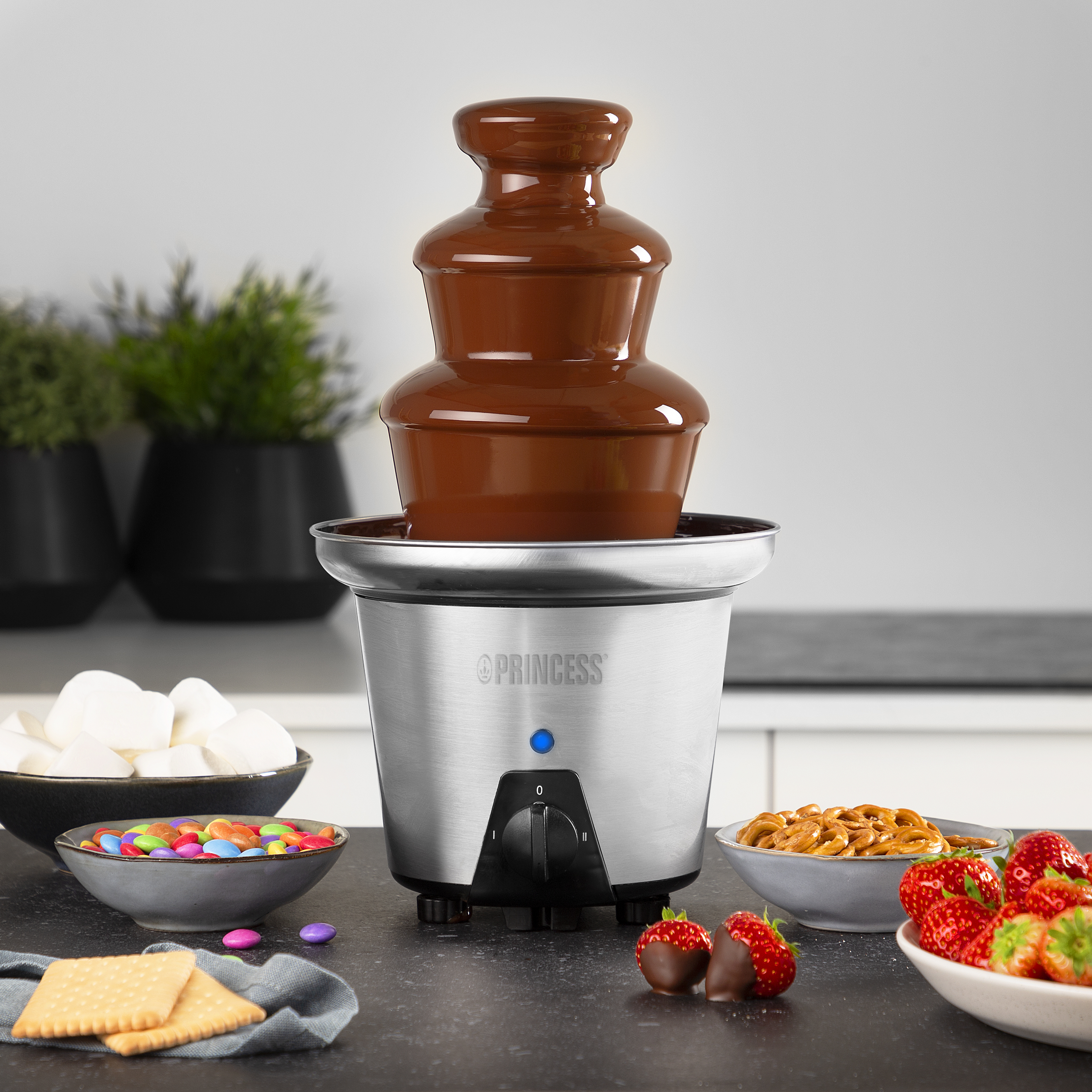 Ein Schokoladenbrunnen mit fließender Schokolade, umgeben von Snacks wie Marshmallows, Keksen und Erdbeeren.