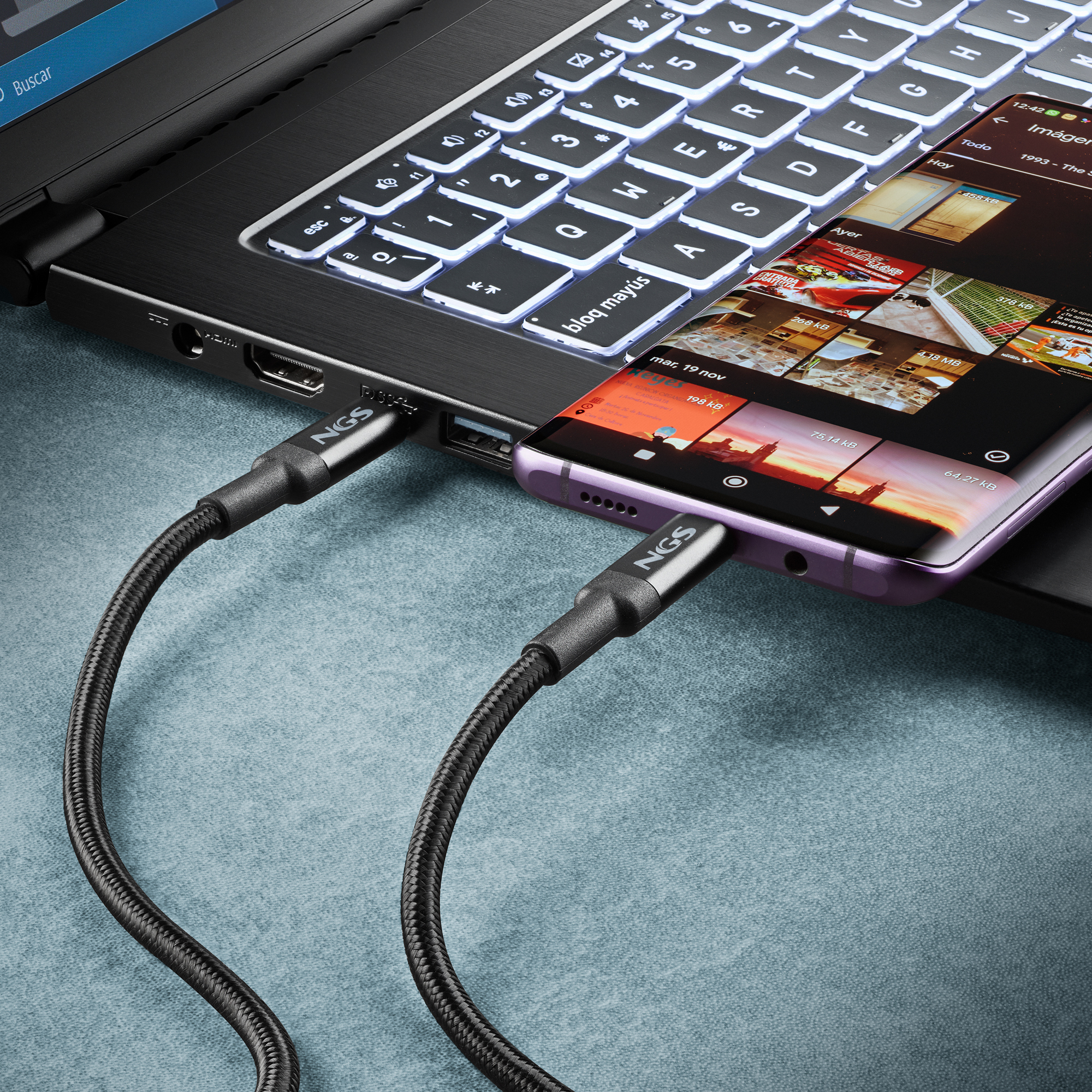 Una laptop y un teléfono conectados por cables de carga. El teléfono muestra imágenes, teclado de la laptop iluminado.