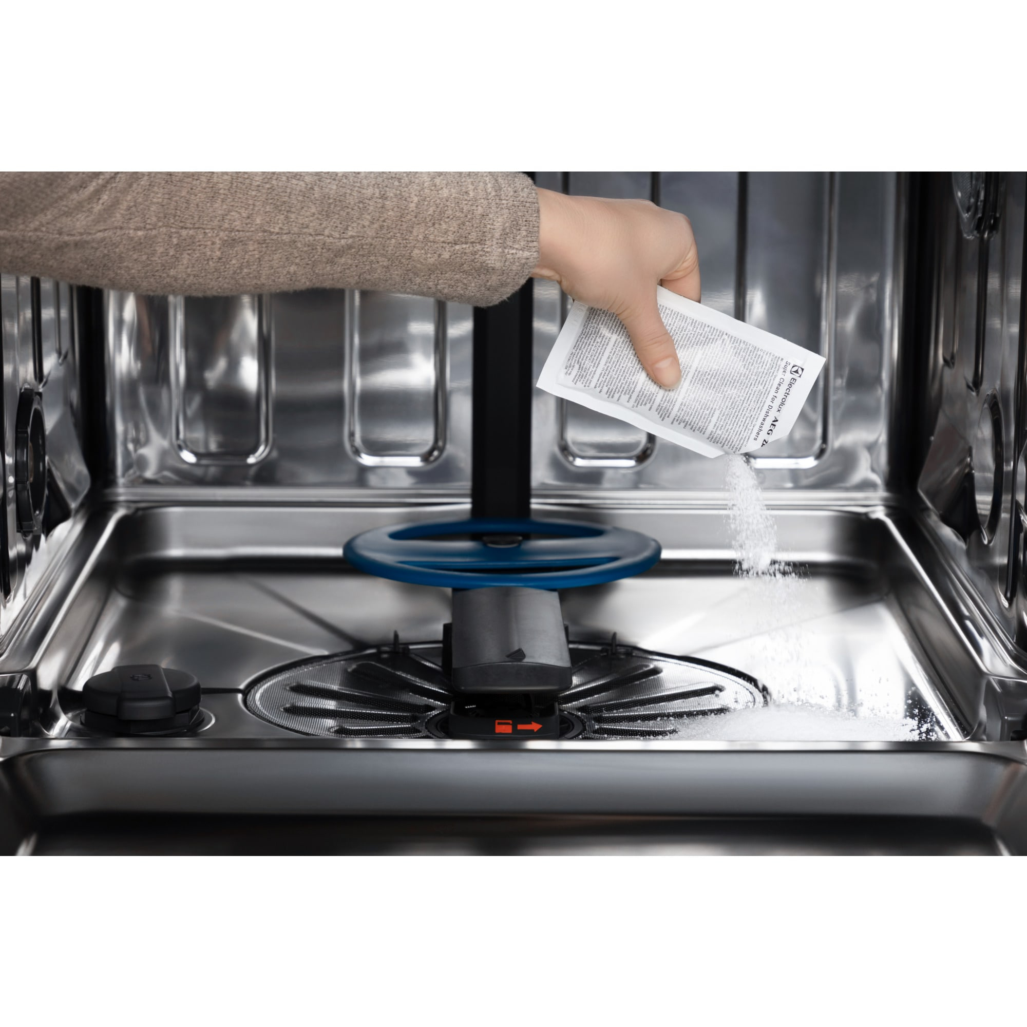 Ręka wlewa środek do czyszczenia zmywarki do urządzenia. Maszyna jest ze stali nierdzewnej, a środek czyszczący to biały proszek.