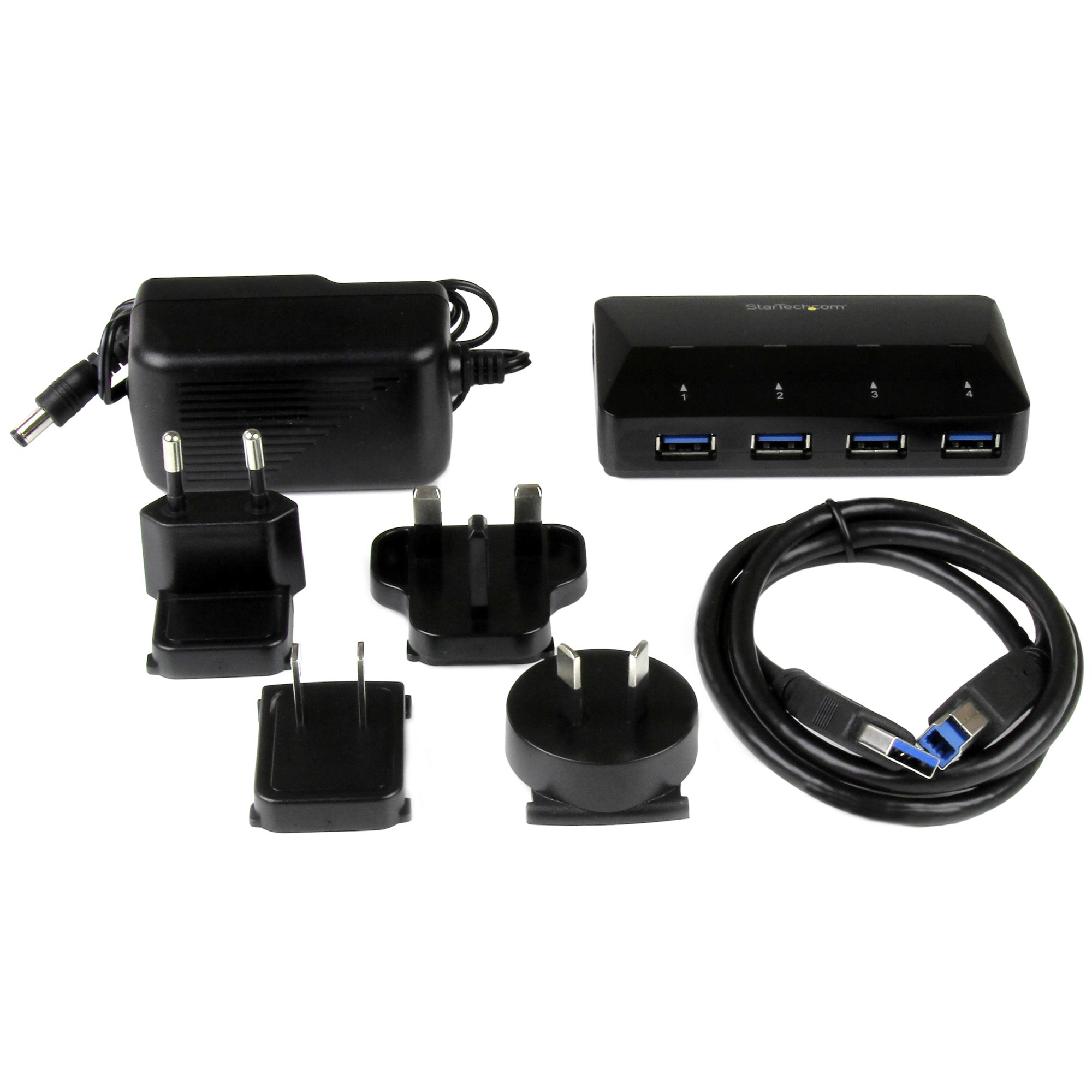 Un concentrador USB negro, un adaptador de corriente y varios adaptadores de enchufe están colocados sobre una superficie blanca. También hay un cable USB.