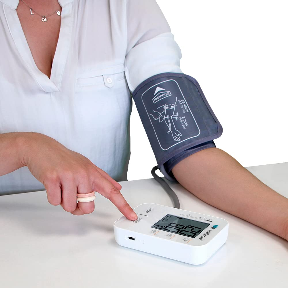 Una persona usa un monitor de presión arterial. El brazalete está en el brazo y la persona presiona el botón de inicio.