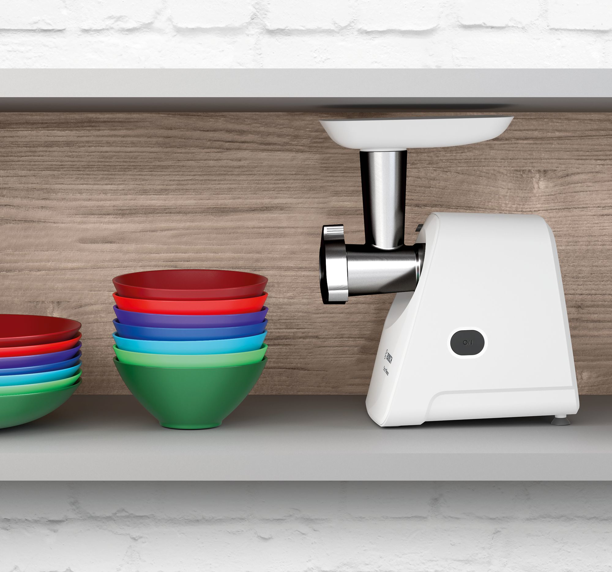 Biała maszynka do mięsa obok stosu kolorowych misek na półce. Tło to drewno i biała ceglana ściana.