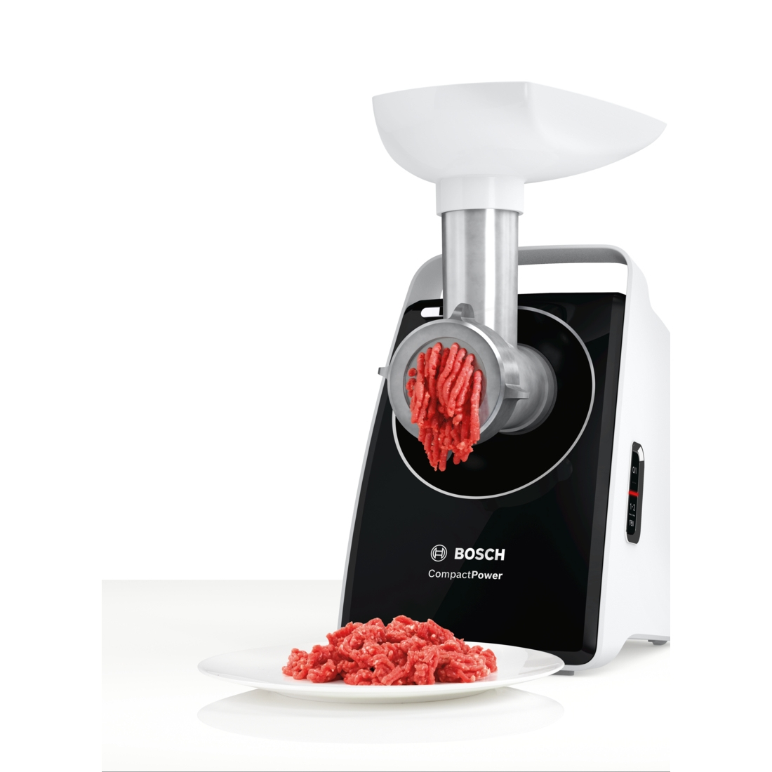Un tritacarne Bosch bianco e nero sta macinando carne rossa. La carne macinata è su un piatto bianco. Lo sfondo è bianco.