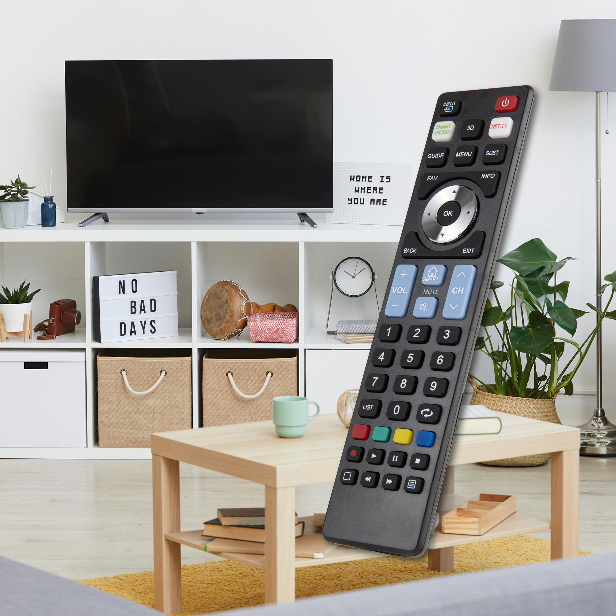 Un telecomando TV è di fronte a un soggiorno con TV, tavolino e mensola decorativa con vari oggetti.