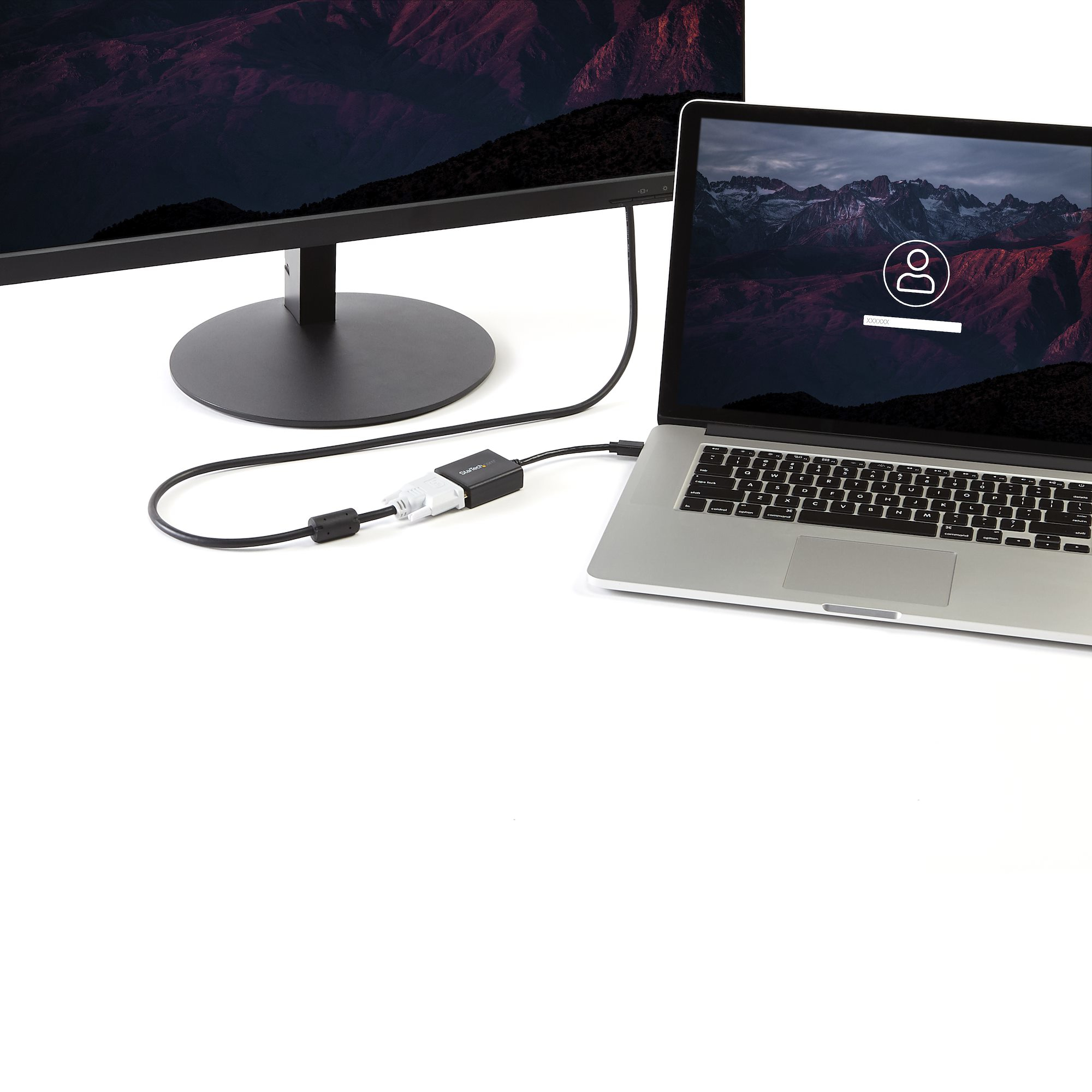 Portátil conectado a un monitor por cable. La pantalla muestra una escena de montaña y un aviso de inicio de sesión.