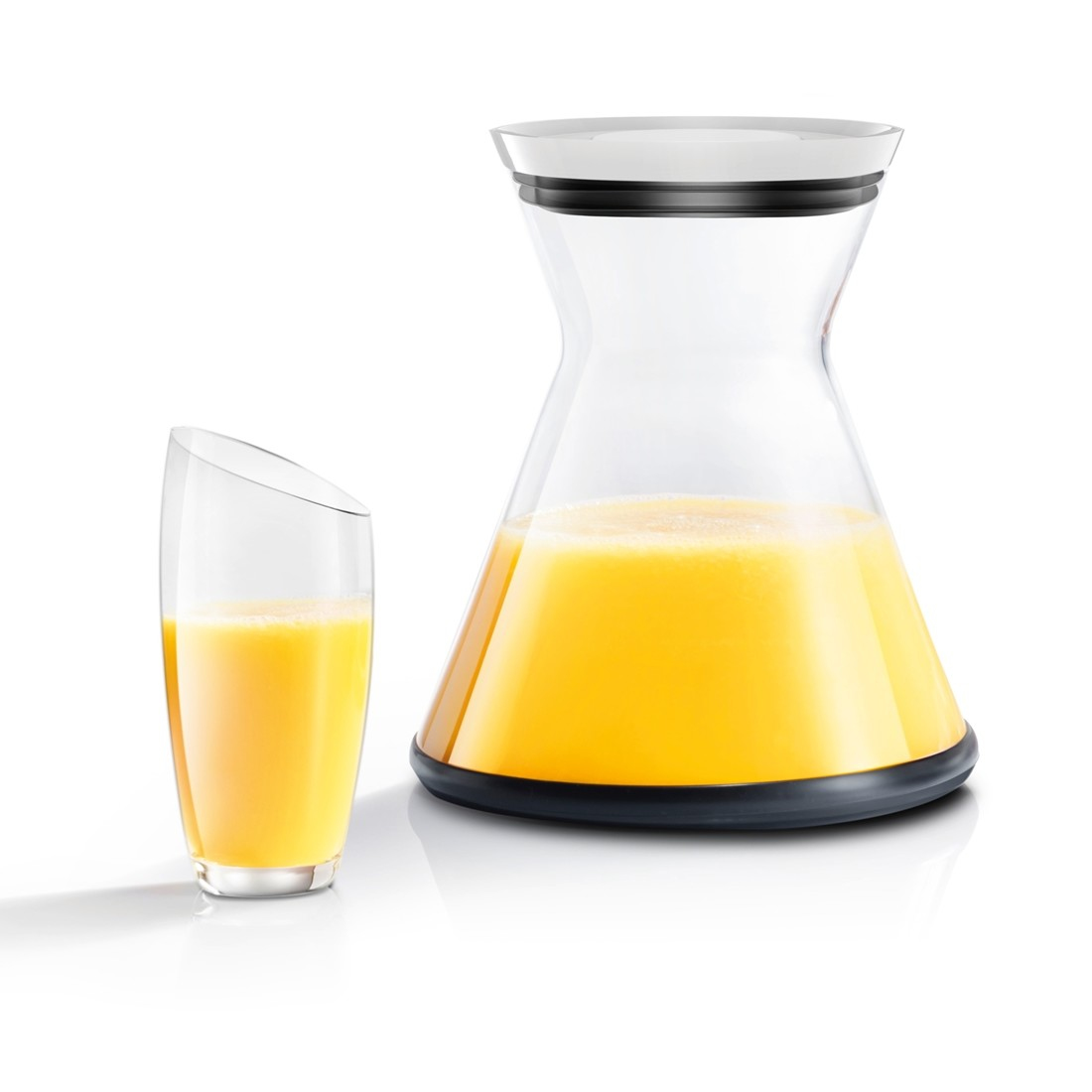 Un vaso y una jarra llenos de zumo de naranja. El vaso a la izquierda, la jarra a la derecha, ambos sobre una superficie blanca.