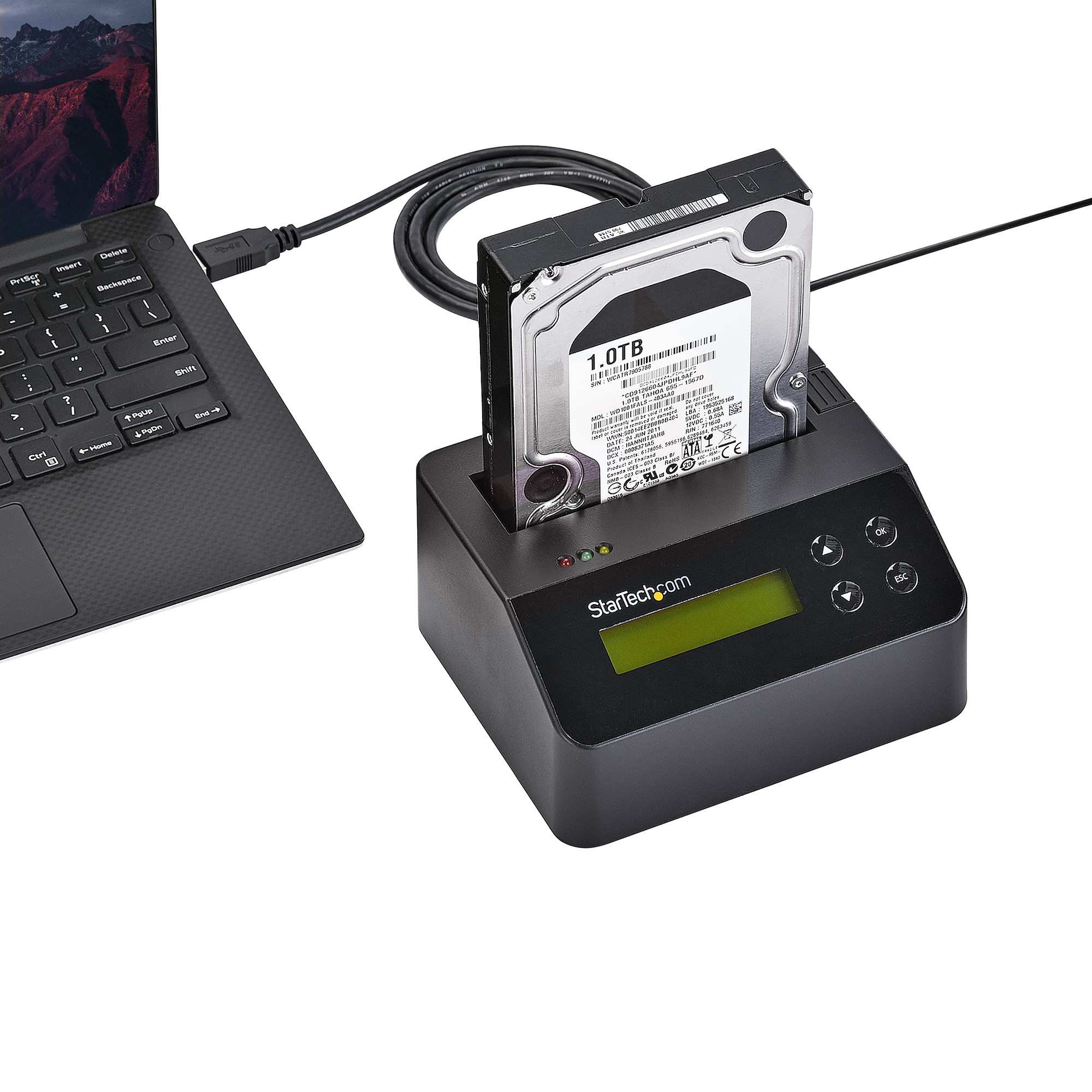 Un disco duro está acoplado en una carcasa negra conectado a una laptop por cable USB. La unidad muestra 1.0TB.