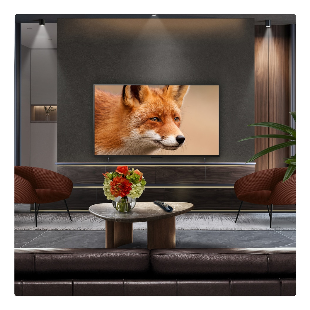 Salon: TV z obrazem lisa, brązowa sofa, krzesła, stolik kawowy z kwiatami i pilot.