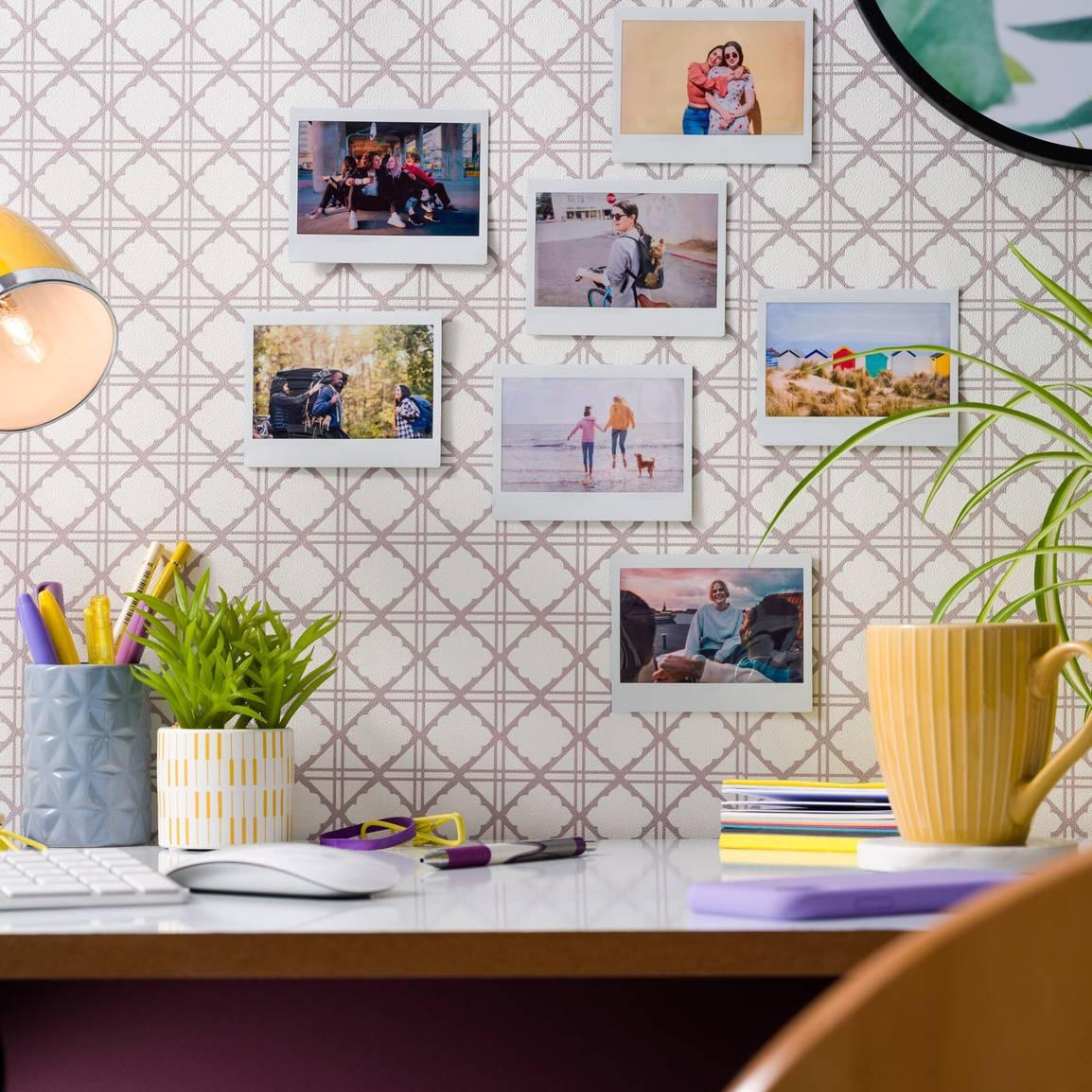 Schreibtisch mit Fotos an einer gemusterten Wand. Enthält eine Tasse, Stifte, Pflanzen und eine Computermaus.
