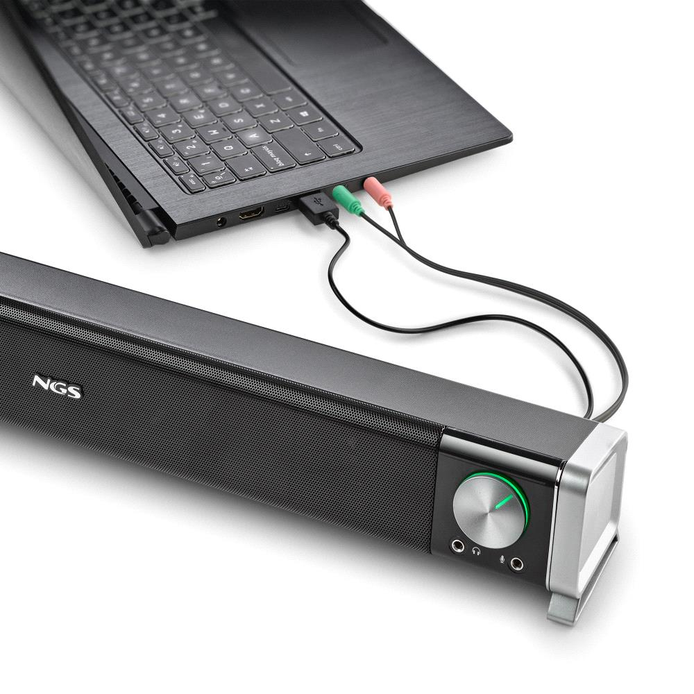 Un laptop collegato a una soundbar nera tramite jack audio verdi e rosa. La soundbar ha una manopola del volume e il marchio NGS.