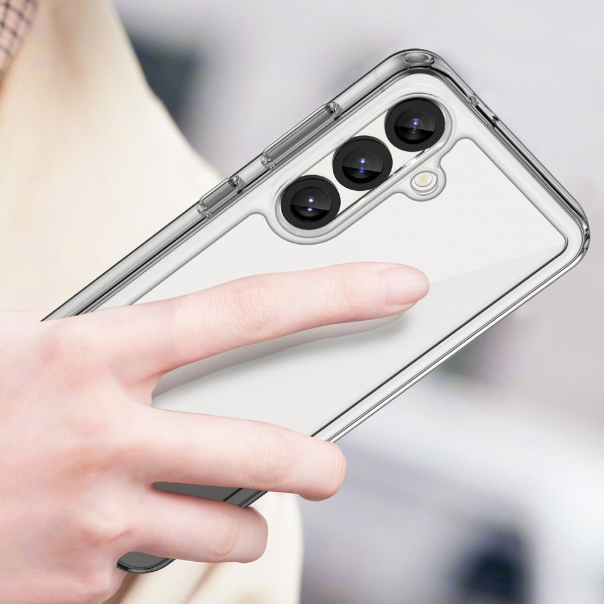 Hand hält eine transparente Handyhülle mit drei Kameralinsen. Die Hülle ist durchsichtig, das Telefon sichtbar. Der Hintergrund ist unscharf.