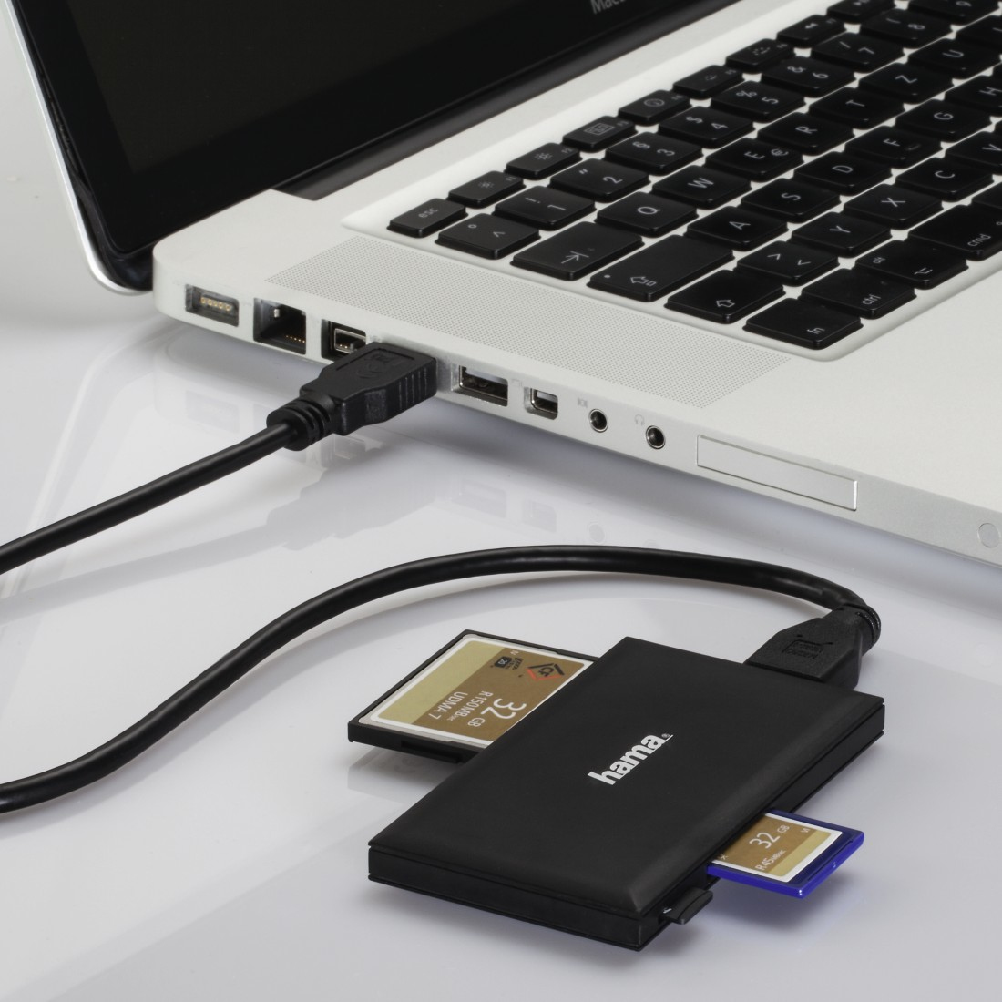 Un laptop con tastiera nera è collegato a un lettore di schede nero con due schede di memoria inserite su una superficie bianca.