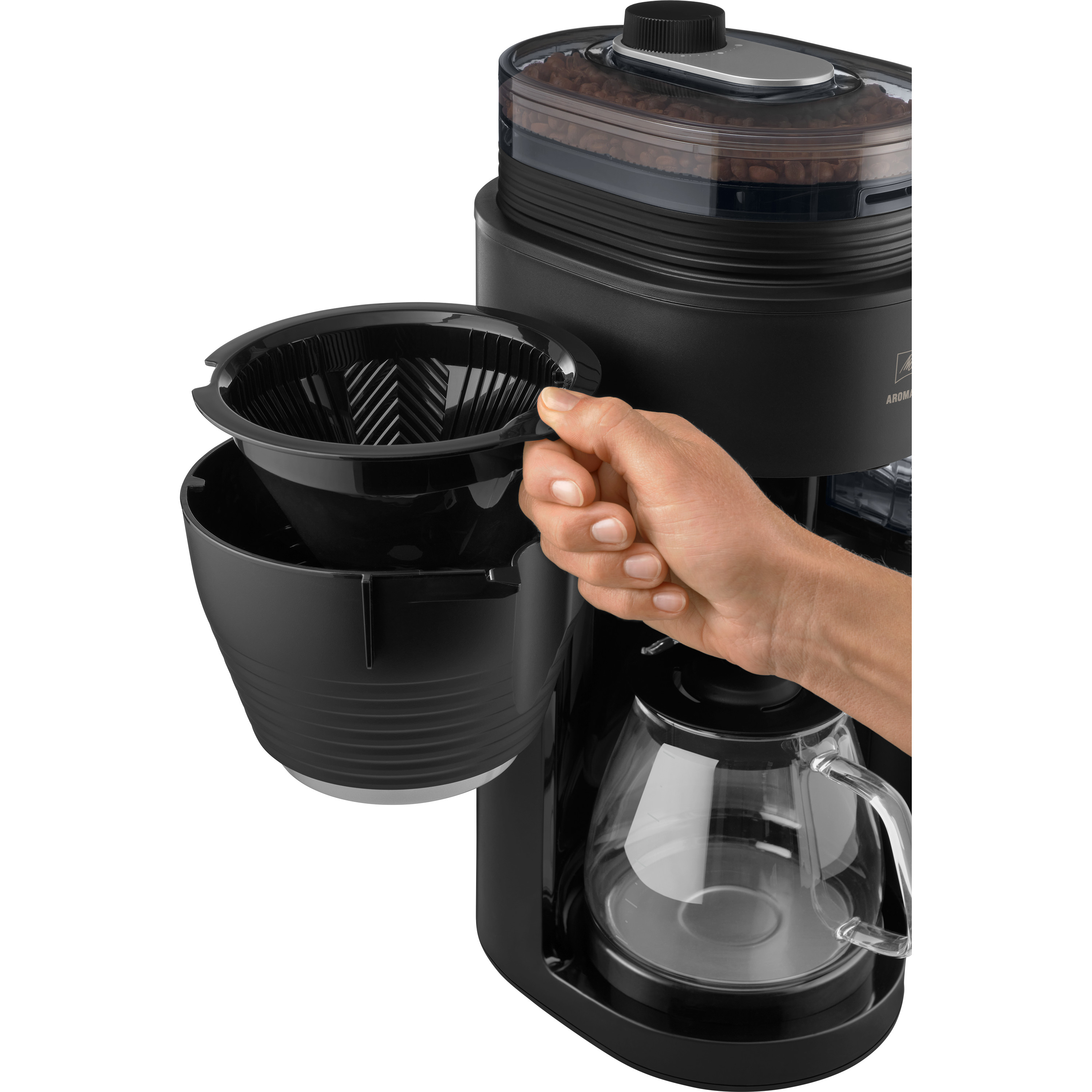 Ręka wkłada czarny filtr do czarnego ekspresu do kawy. Ziarna kawy widoczne w górnym pojemniku, szklana karafka na dole.