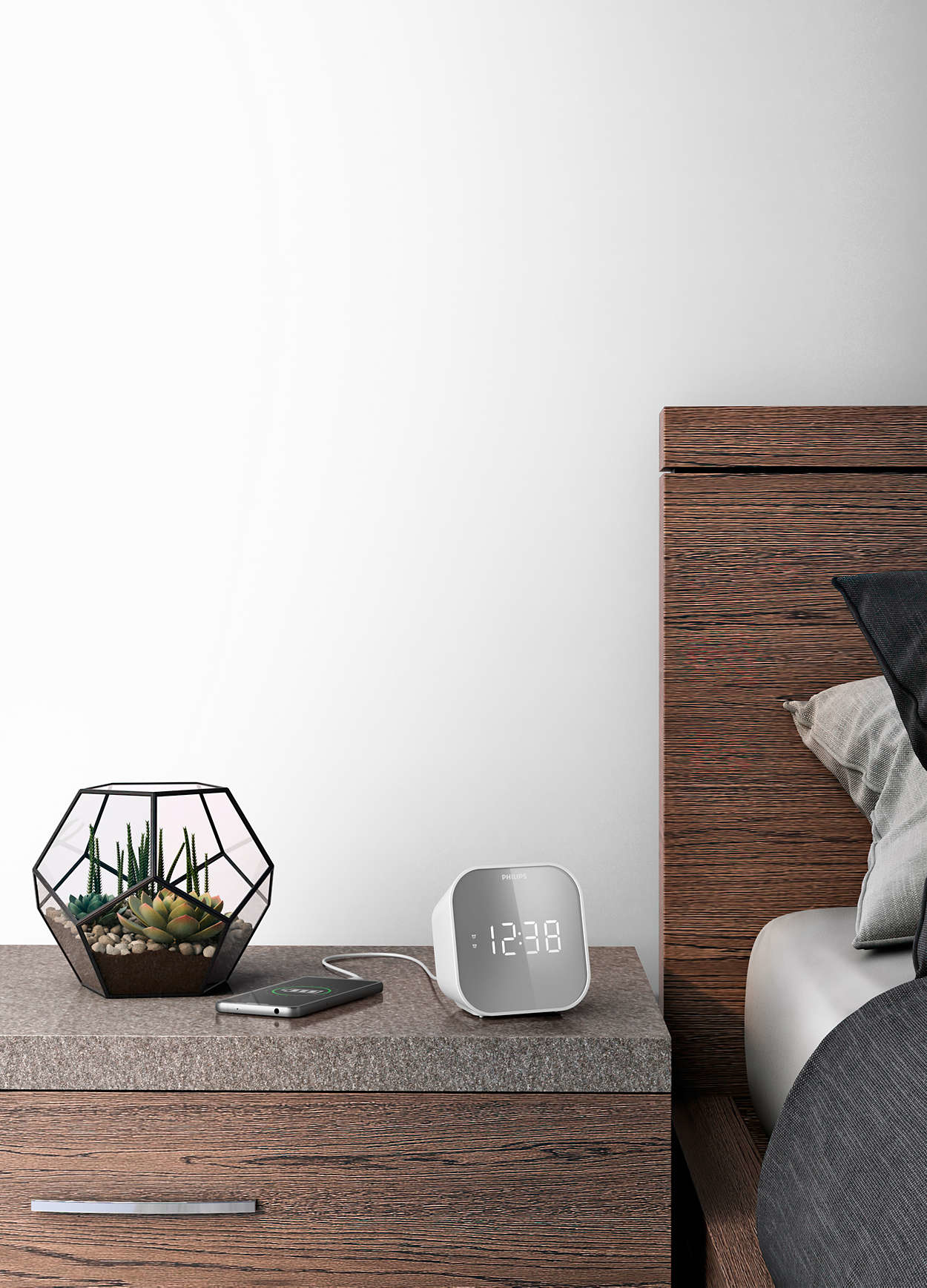 Una mesita de noche con un terrario, reloj y teléfono. Una cama está a la derecha. El reloj marca las 12:38.