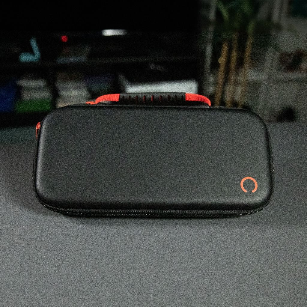 A black case with an orange handle and a 'C' logo. It's on a gray surface, with a dark blurred background.