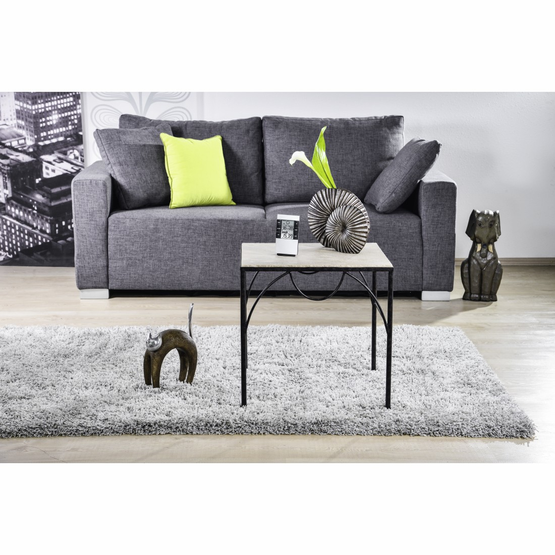 Szara sofa z limonkową poduszką, stolik kawowy, puszysty dywan i przedmioty dekoracyjne. Posąg kota i psa.