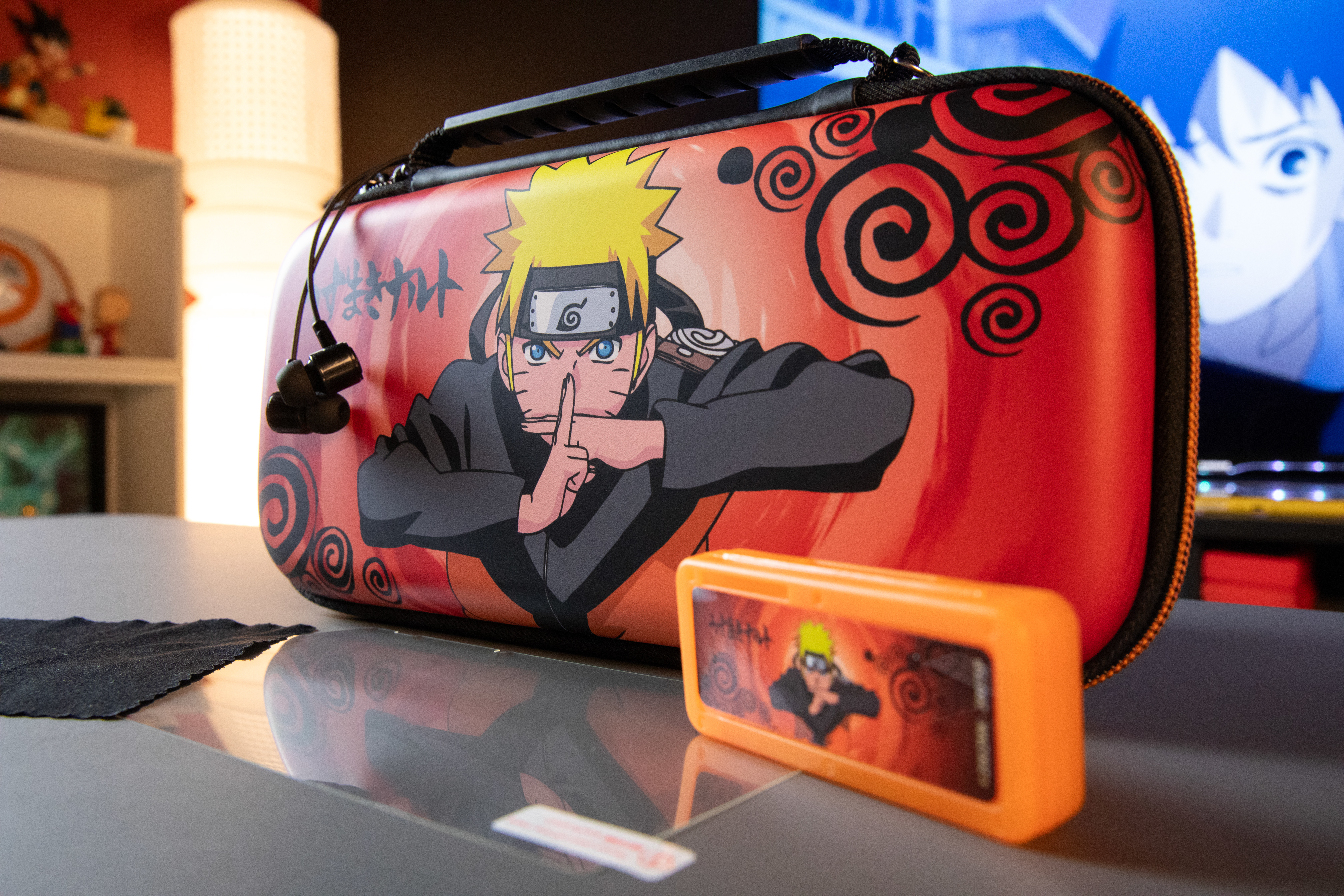 Na stole leżą etui z motywem Naruto i pomarańczowe pudełko. Etui przedstawia Naruto. Wiszą na nim słuchawki.