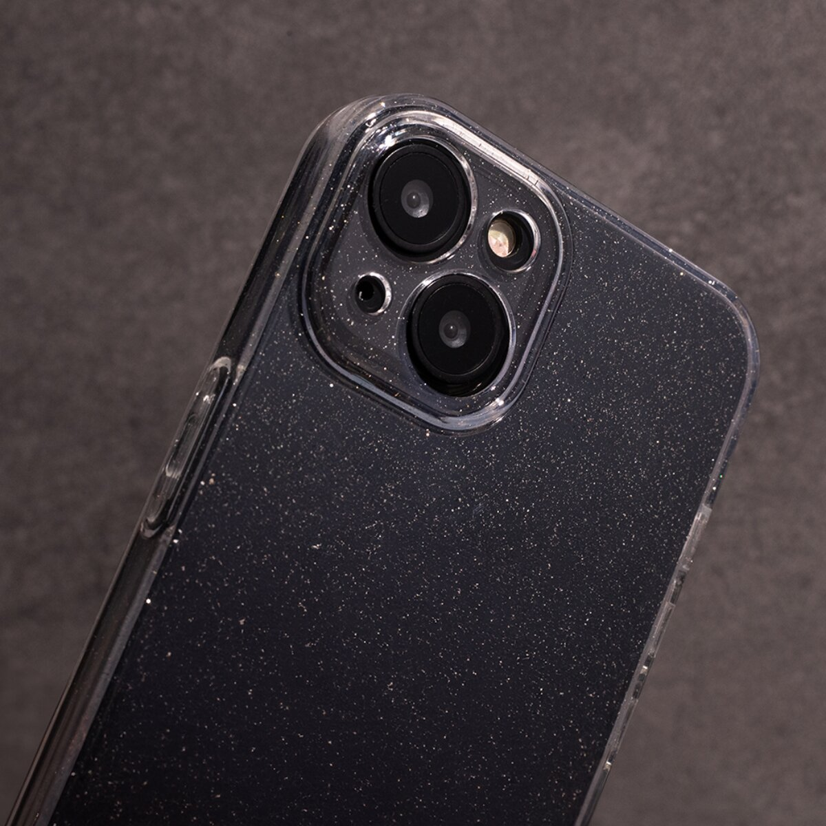 Nahaufnahme eines schwarzen Smartphones mit Glitzereffekt und drei Kameralinsen. Der Hintergrund ist eine dunkelgraue Oberfläche.