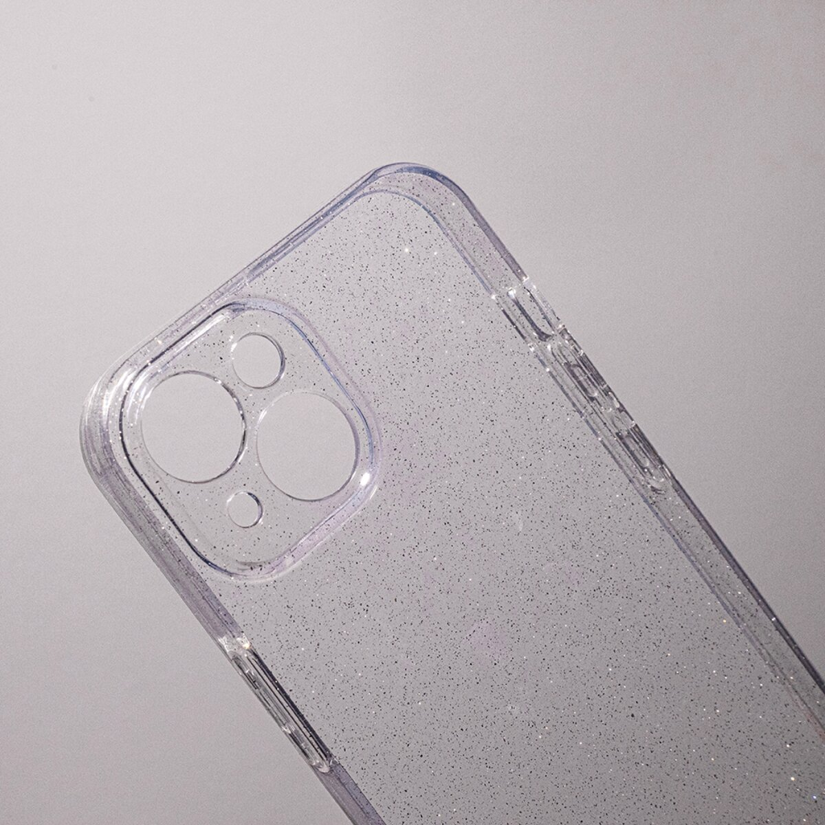 Transparente, glitzerbesetzte Handyhülle, schräge Ansicht. Mit Kameraausschnitten und Seitentasten. Hintergrund ist eine schlichte, hellgraue Oberfläche.