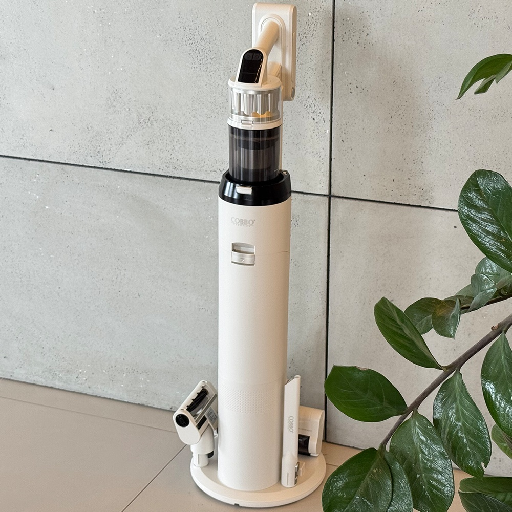 Biały odkurzacz bezprzewodowy jest zamontowany na ścianie. Ma czarny i przezroczysty pojemnik na kurz. Akcesoria są na podstawie.