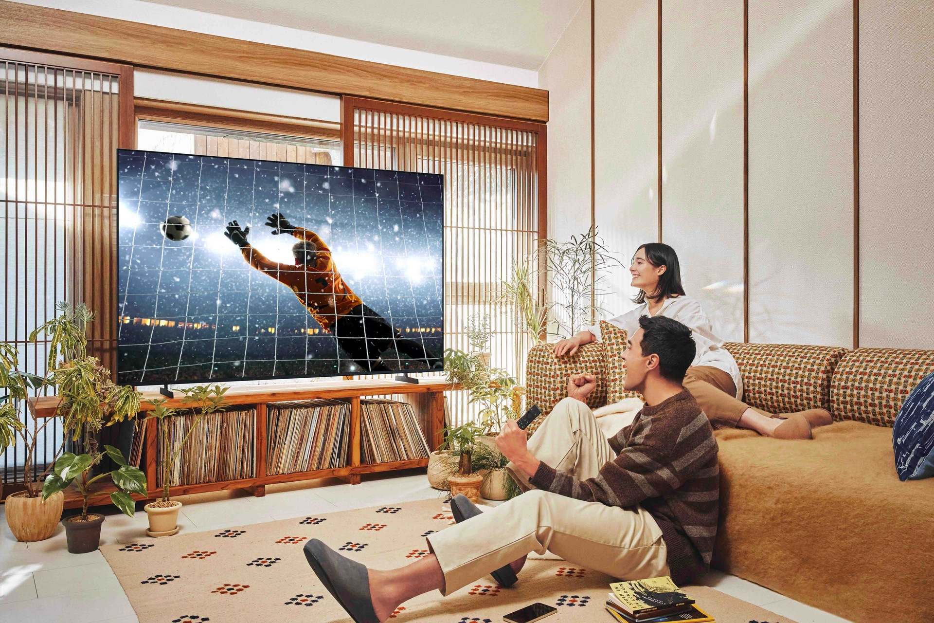 Para ogląda piłkę nożną w telewizji. Telewizor pokazuje bramkarza próbującego zablokować piłkę nożną. Są w nowoczesnym salonie.