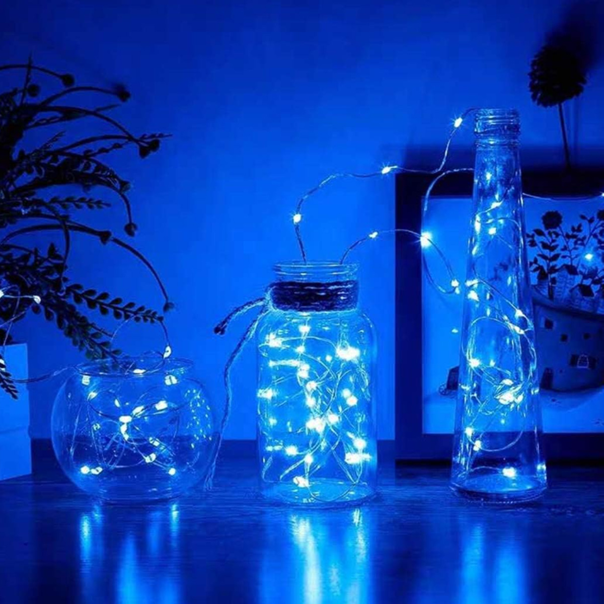 Drei Glasbehälter mit blauen Lichterketten. Die Szene wird von blauem Licht beleuchtet, wodurch ein weiches, umgebendes Leuchten entsteht.
