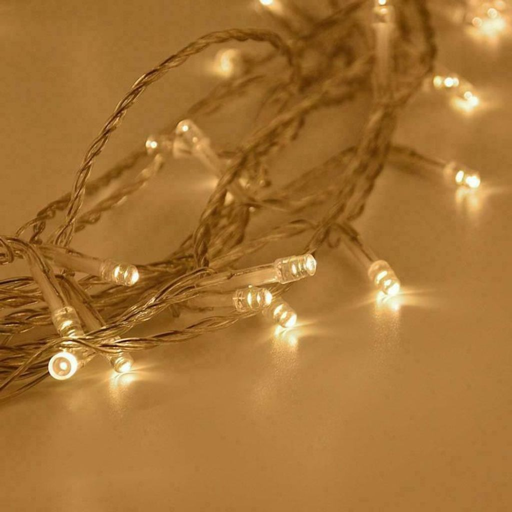 Nahaufnahme von Lichterketten mit kleinen, warmweißen LEDs. Die Drähte sind silbern, der Hintergrund ist weich gelb.