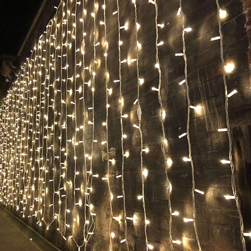 Eine Wand aus warmweißen Lichterketten hängt vor einer dunklen Backsteinmauer. Die Lichter sind gleichmäßig verteilt und beleuchtet.