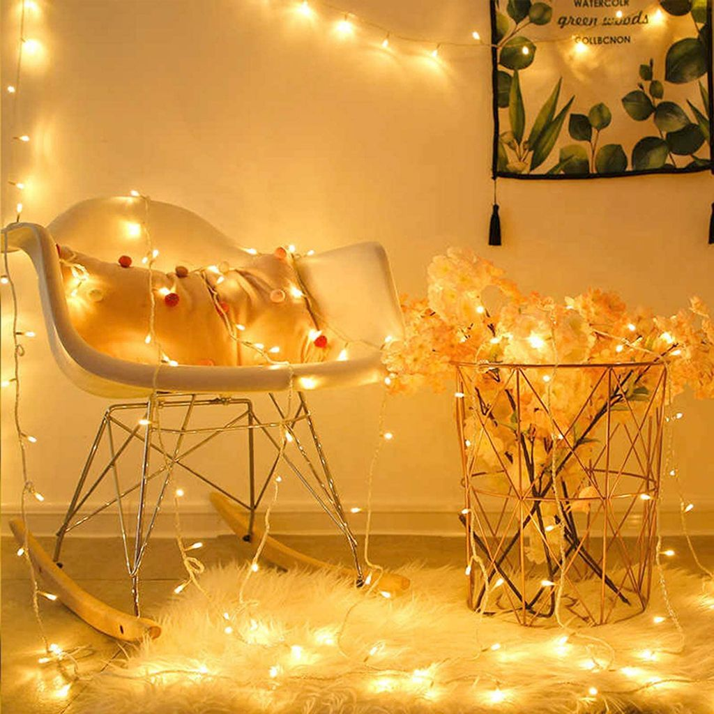 Ein weißer Stuhl mit Kissen und Lichtern, ein goldener Drahtkorb mit Blumen und ein flauschiger Teppich.