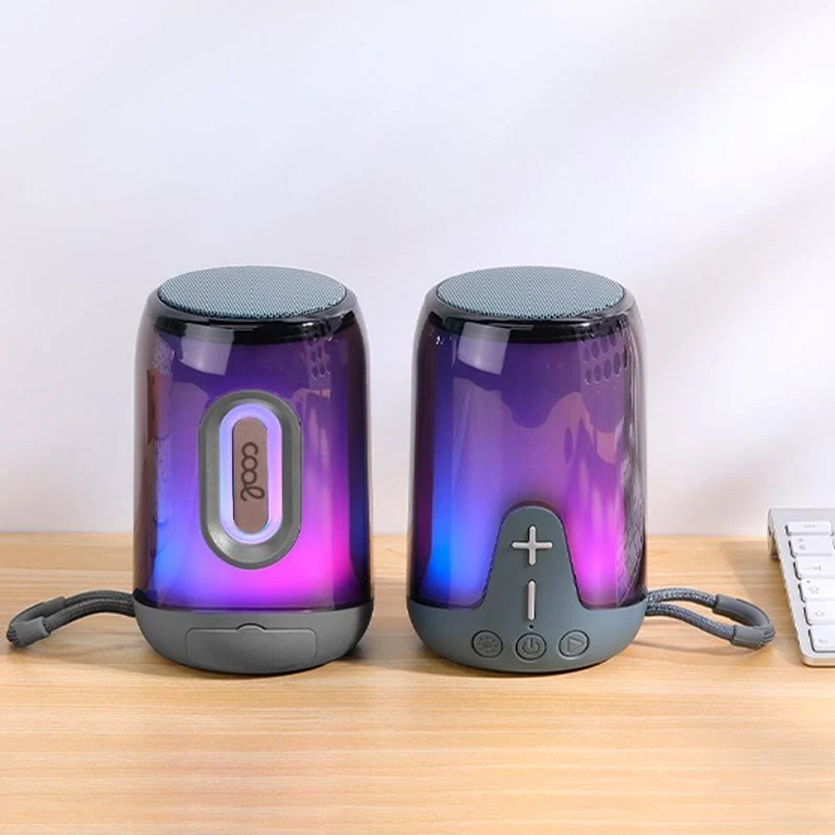 Dos altavoces cilíndricos con efectos de luz púrpura y azul, bases y tapas grises, sobre una superficie de madera.