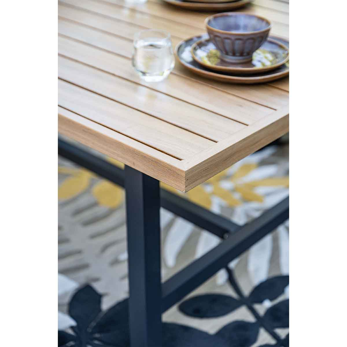 Table en bois avec un bol, des assiettes et un verre d'eau. La table a des pieds en métal noir. Un tapis à motifs en dessous.