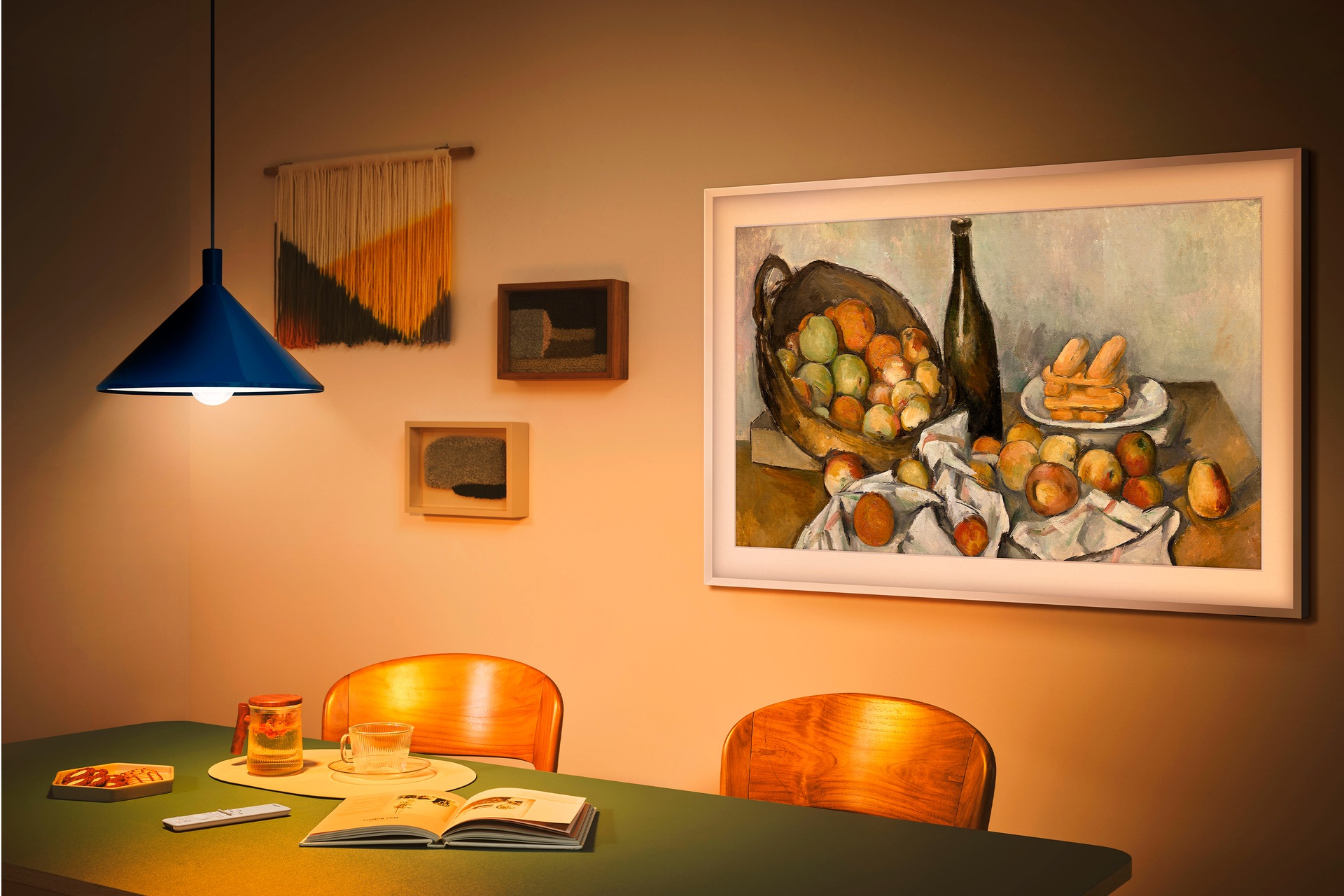 Scena jadalniana z obrazem owoców, stołem z napojami i książkami oraz niebieską lampą.