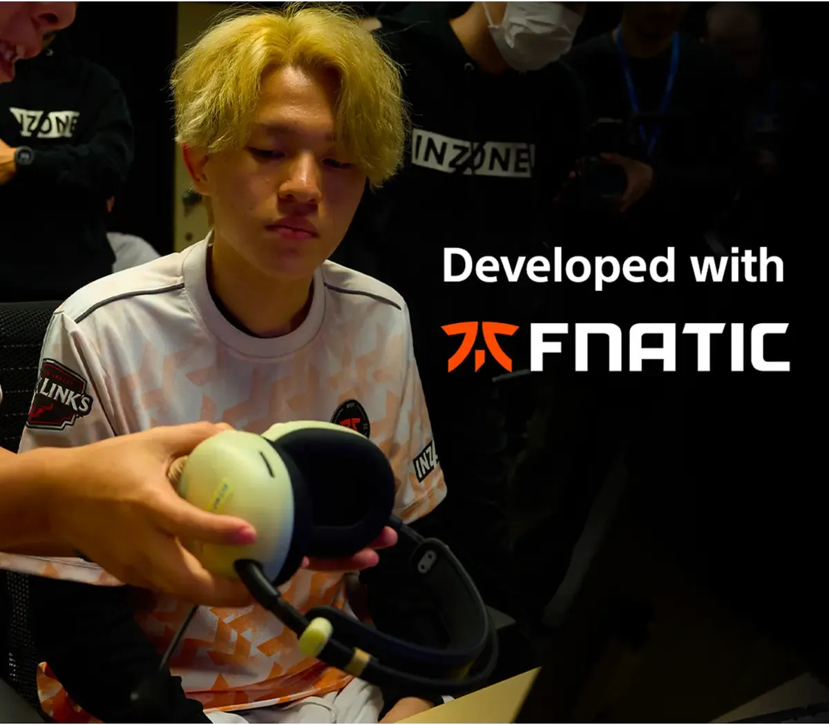 Un jeune homme aux cheveux blonds reçoit un casque. Il porte une chemise avec un logo. Le fond montre les logos INZONE et FNATIC.