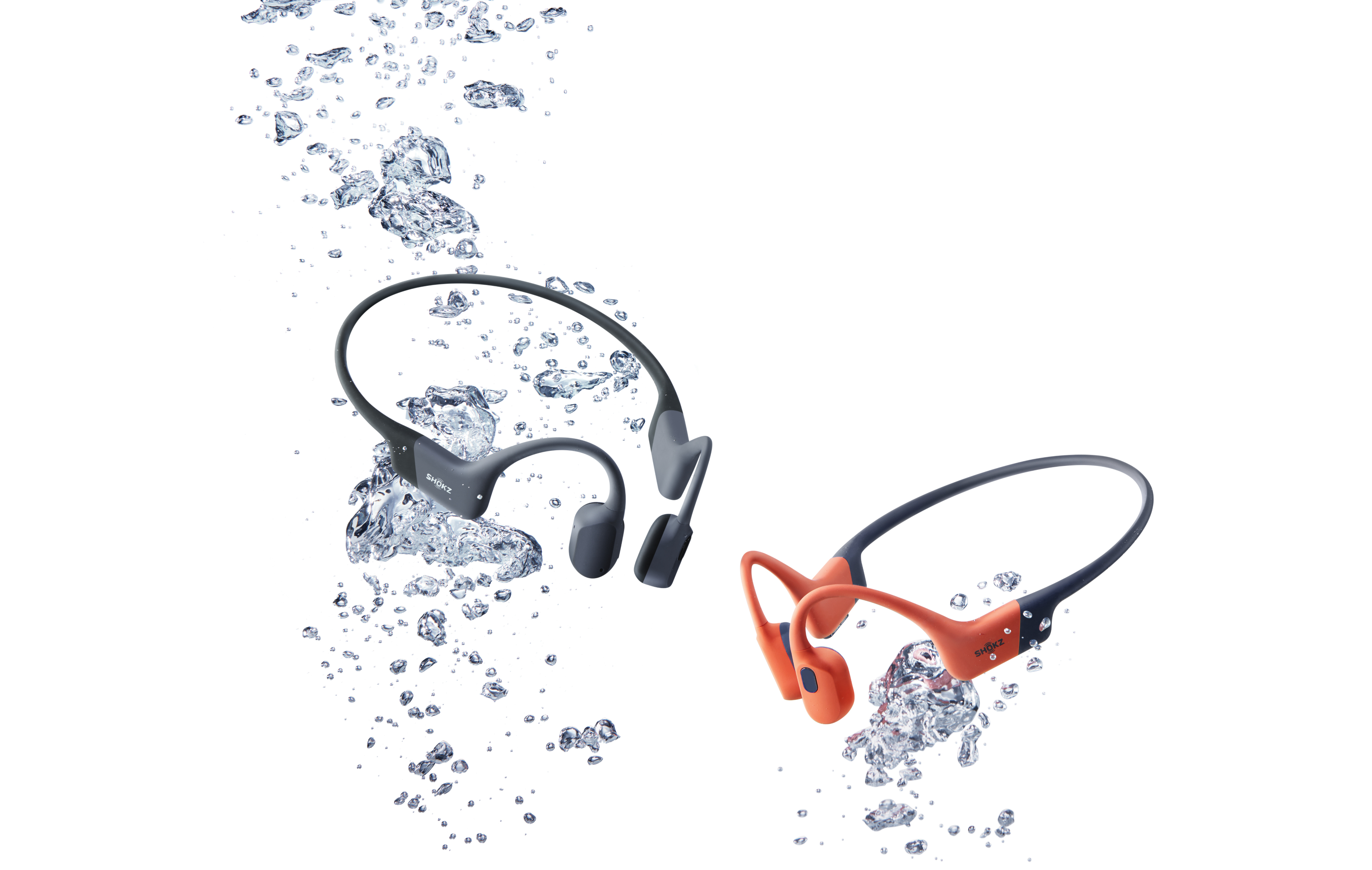 Deux écouteurs à conduction osseuse, un gris, un orange, entourés de bulles d'eau, sur fond blanc.