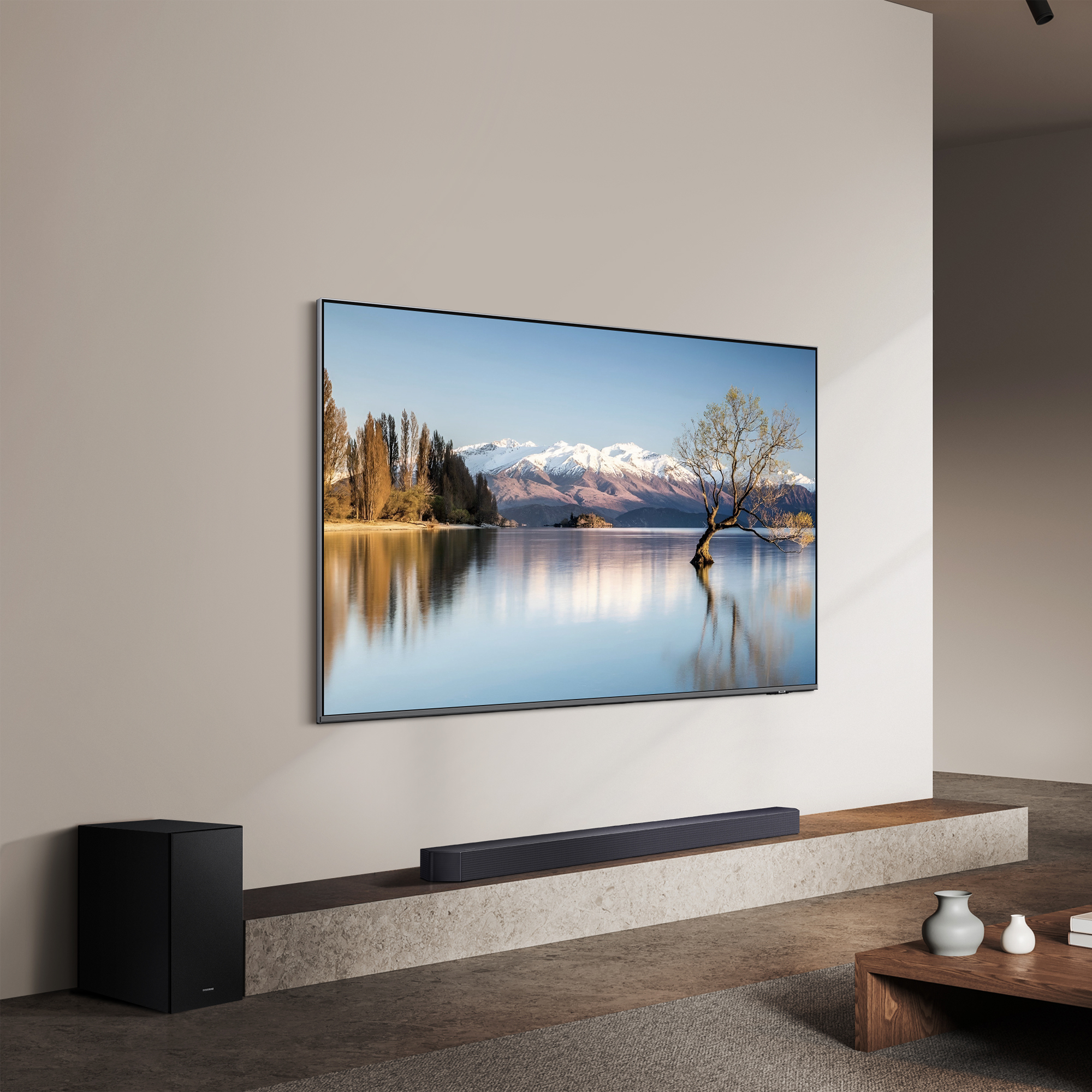 Ein Fernseher zeigt eine Seeszene mit Bergen, einem Baum und einer Soundbar. Auf der linken Seite befindet sich ein Subwoofer.