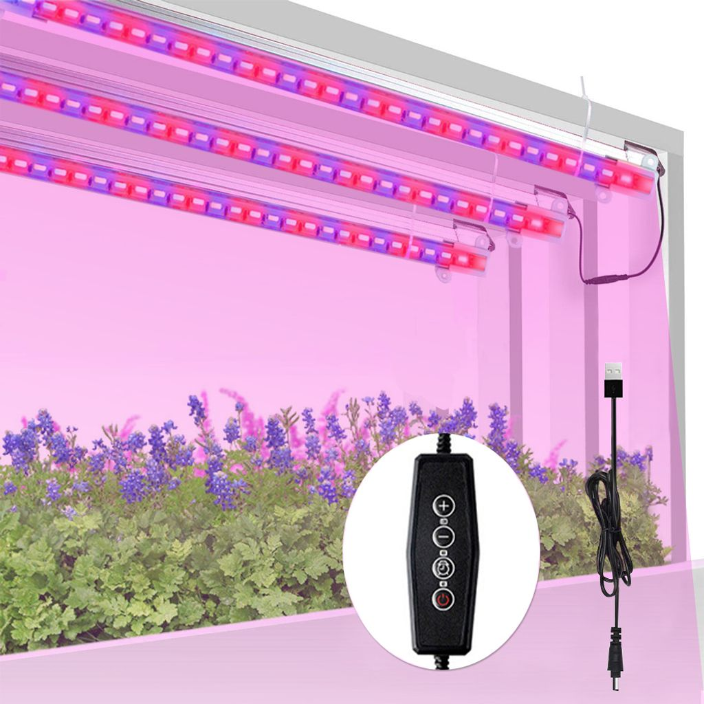 LED-Pflanzenleuchten über Pflanzen. Lila und rote Lichter. Bedienfeld und USB-Kabel. Blumen und grüne Pflanzen im Vordergrund.
