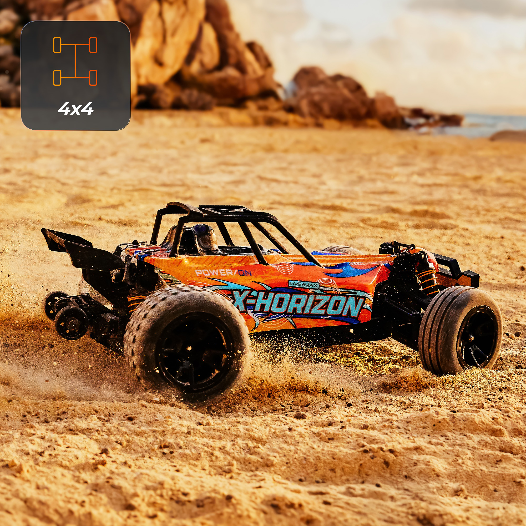 Een oranje en blauwe 4x4 RC-auto op een zandstrand, dat zand opwaait. Rotsen en oceaan op de achtergrond.