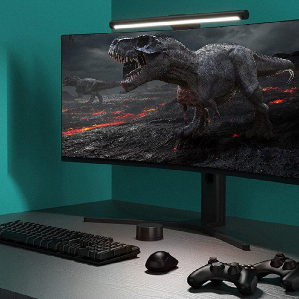 Ein Computermonitor zeigt eine Dinosaurierszene. Tastatur, Maus und Gamecontroller liegen auf dem Schreibtisch, unter einer Schreibtischlampe.
