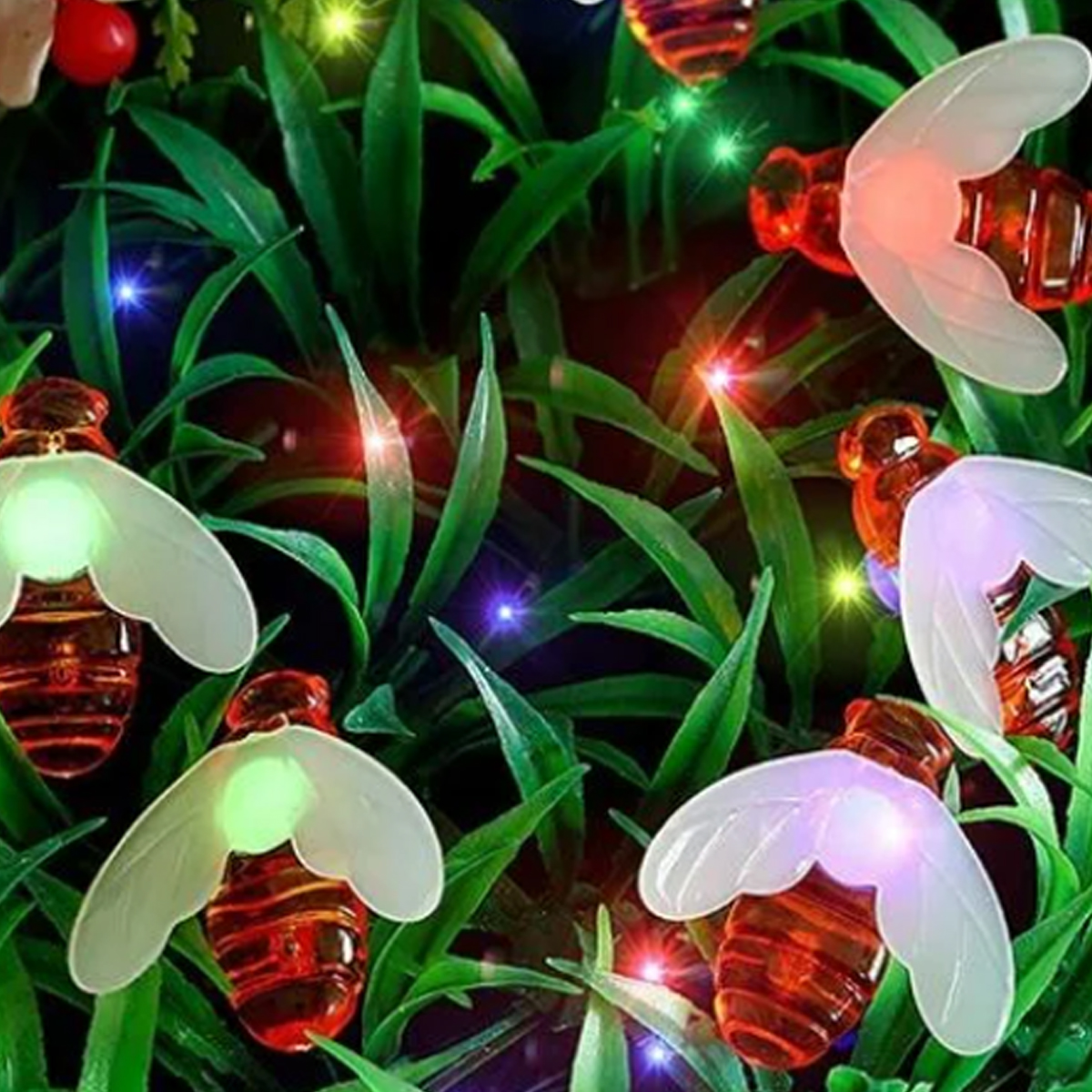 Dekorative Lichter in Form von Bienen mit leuchtenden Flügeln. Sie sind von grünen Blättern umgeben. Winzige bunte Lichter sind verstreut.