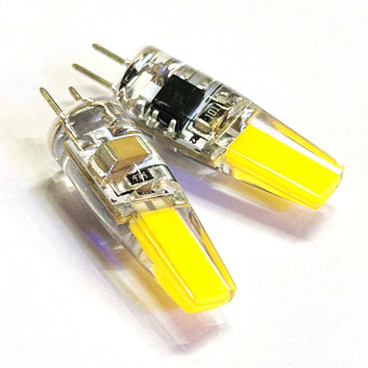 Zwei transparente LED-Glühbirnen mit gelben lichtemittierenden Teilen und Metallstiften auf weißem Hintergrund.