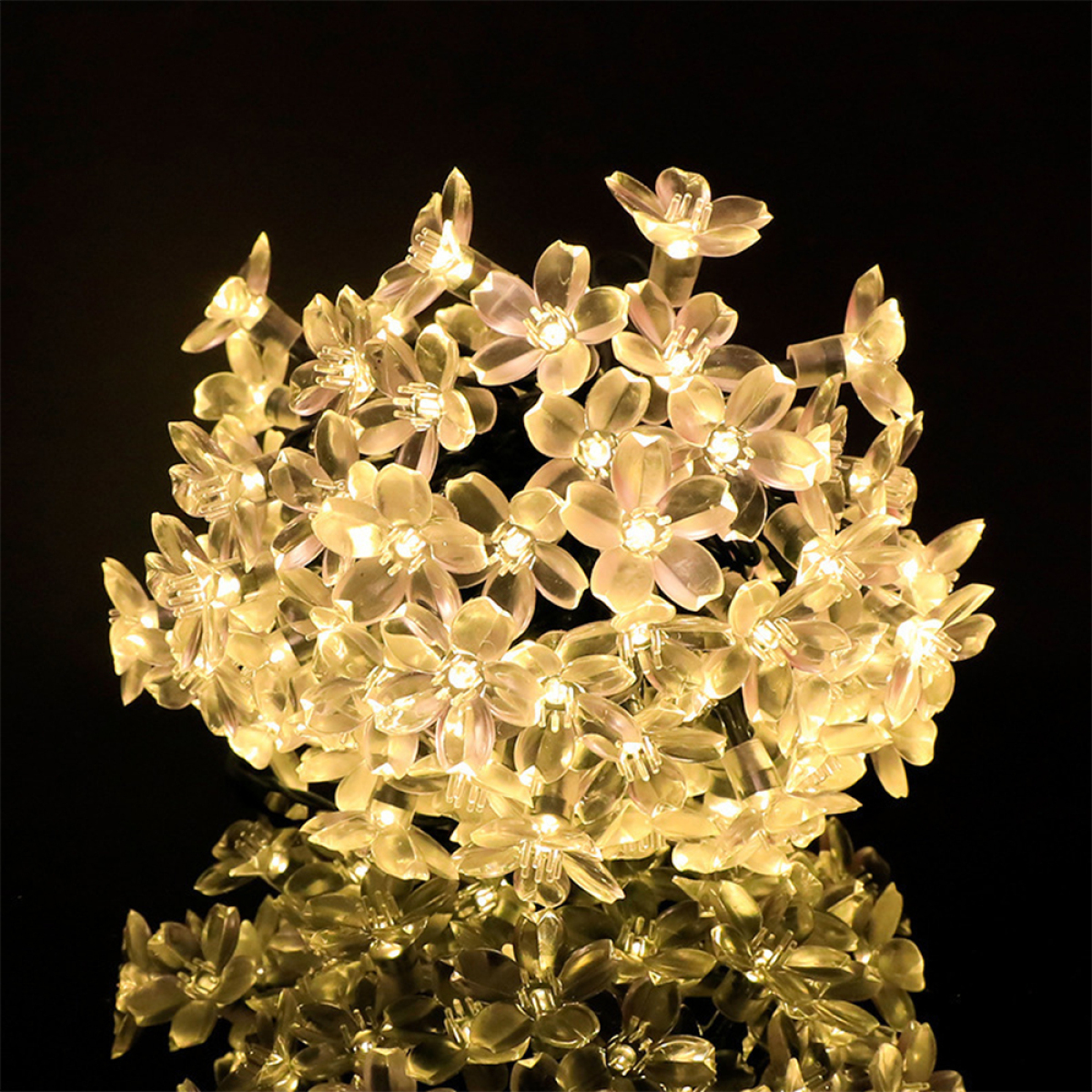 Ein Cluster aus leuchtenden, transparenten Blumenlichtern vor dunklem Hintergrund, die sich in einer glänzenden Oberfläche spiegeln.