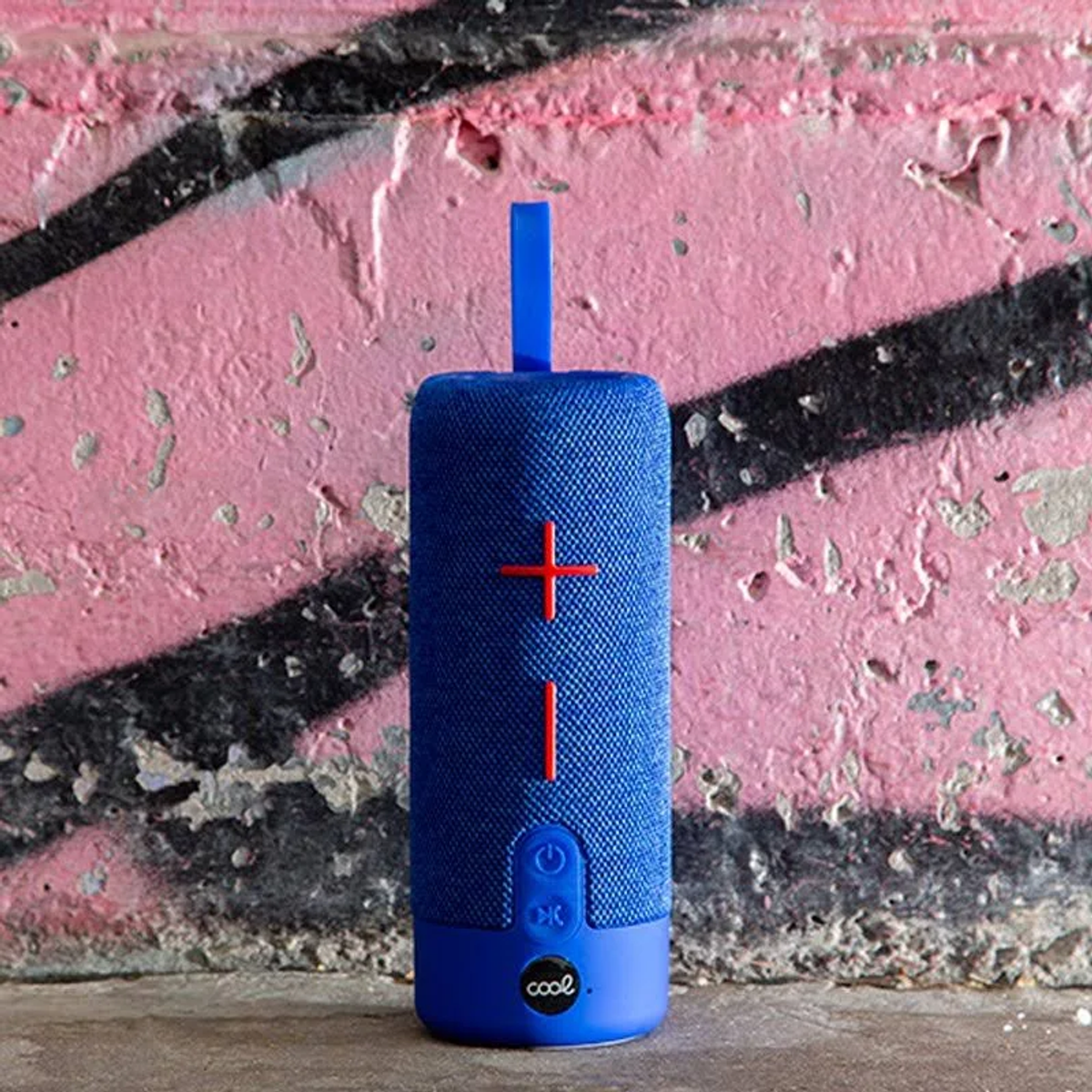 Niebieski głośnik z czerwonym krzyżem na tle różowej i czarnej ściany z graffiti.