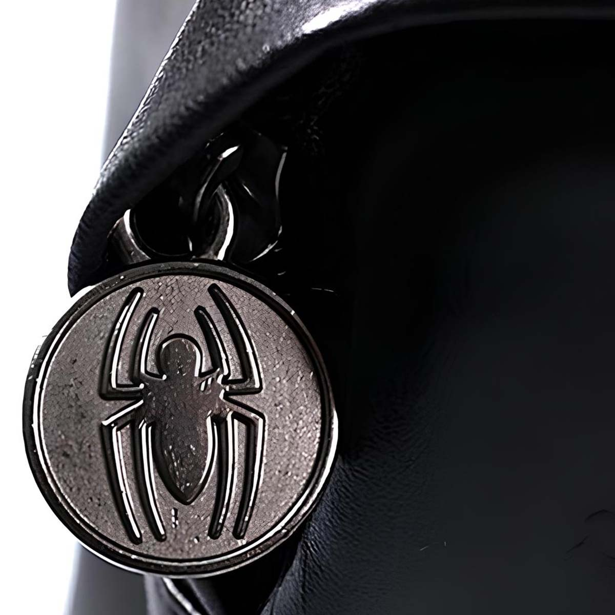 Primo piano di un emblema argentato di Spider-Man su sfondo nero, probabilmente parte di una borsa o accessorio.