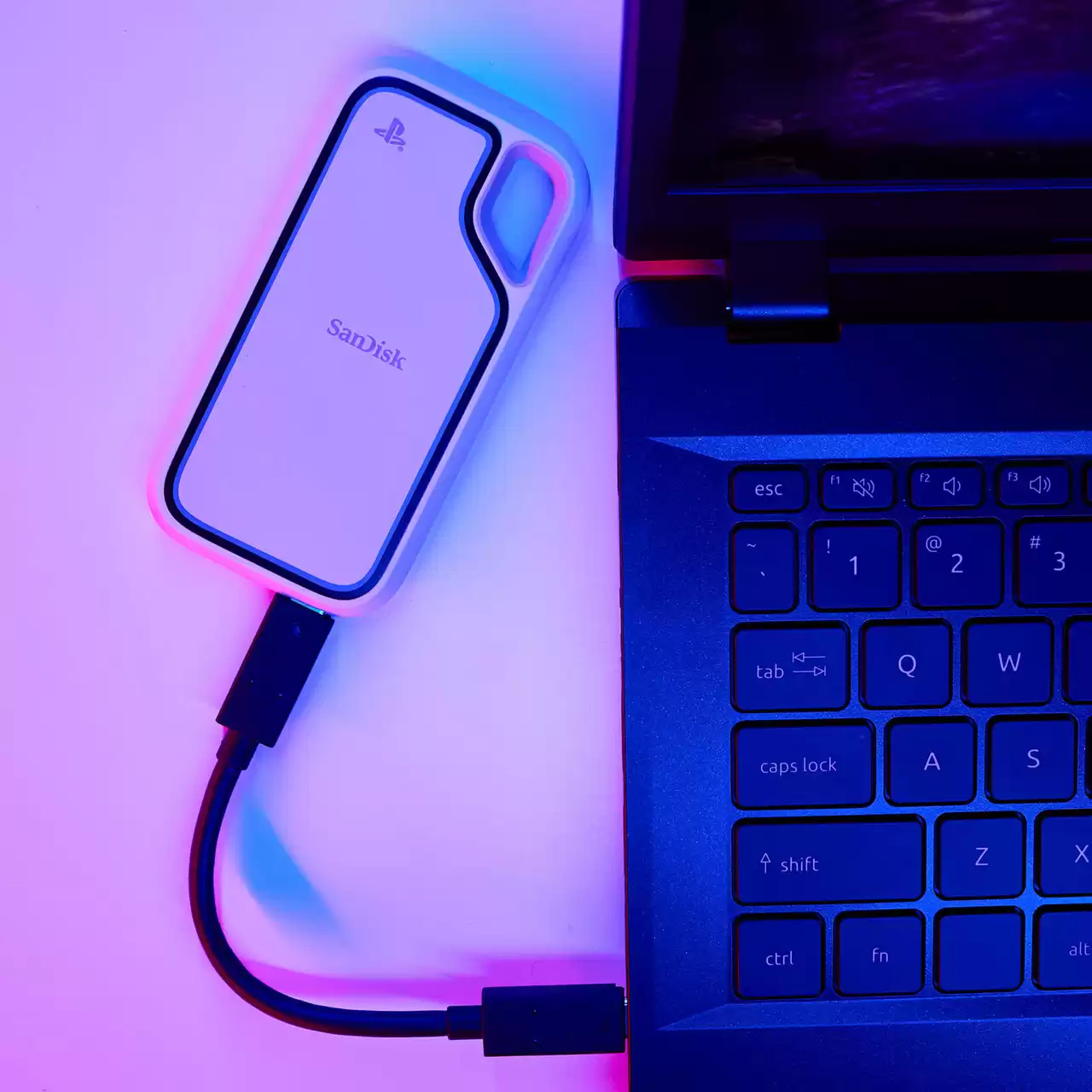 Biały zewnętrzny dysk twardy SanDisk jest podłączony do laptopa. Klawiatura jest niebieska. Tło ma fioletowe i niebieskie odcienie.