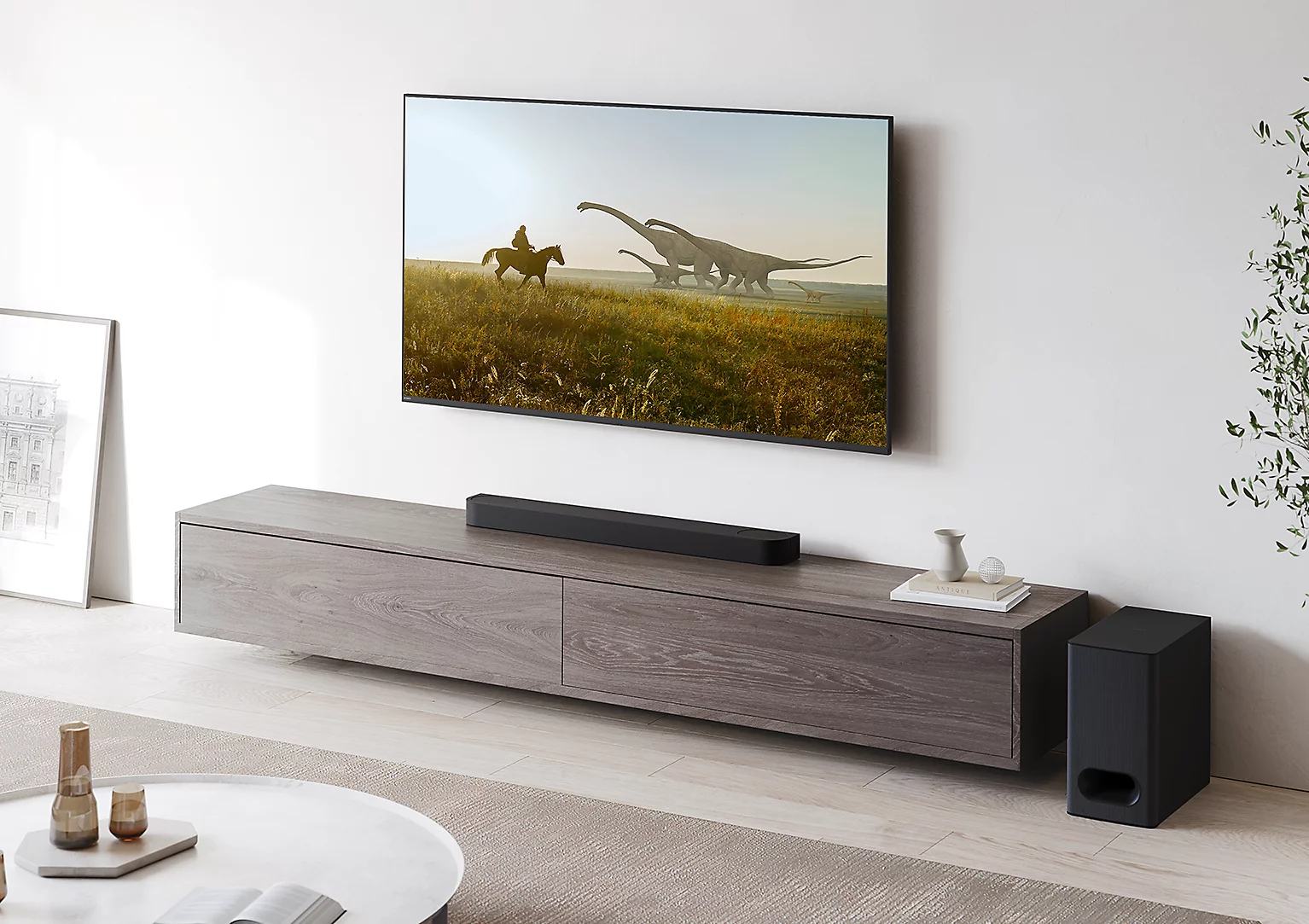 Ein Fernseher zeigt eine Dinosaurierszene. Darunter ist eine Soundbar. Ein Pferd und Reiter sind auf dem Bildschirm.