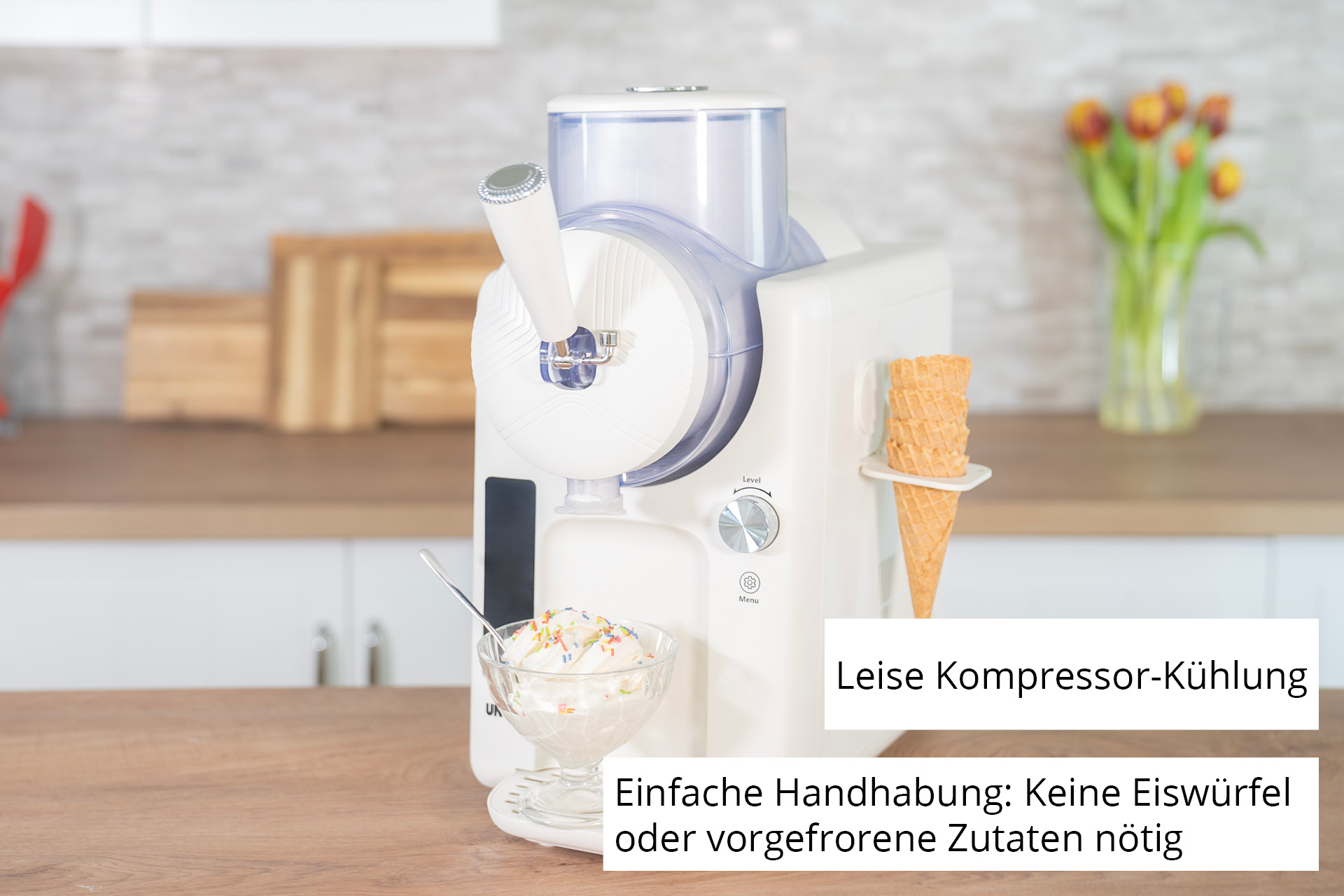 Eine Eismaschine mit einer Schüssel Eis, Waffelhörnchen und einer Blumenvase auf einer Holzoberfläche.