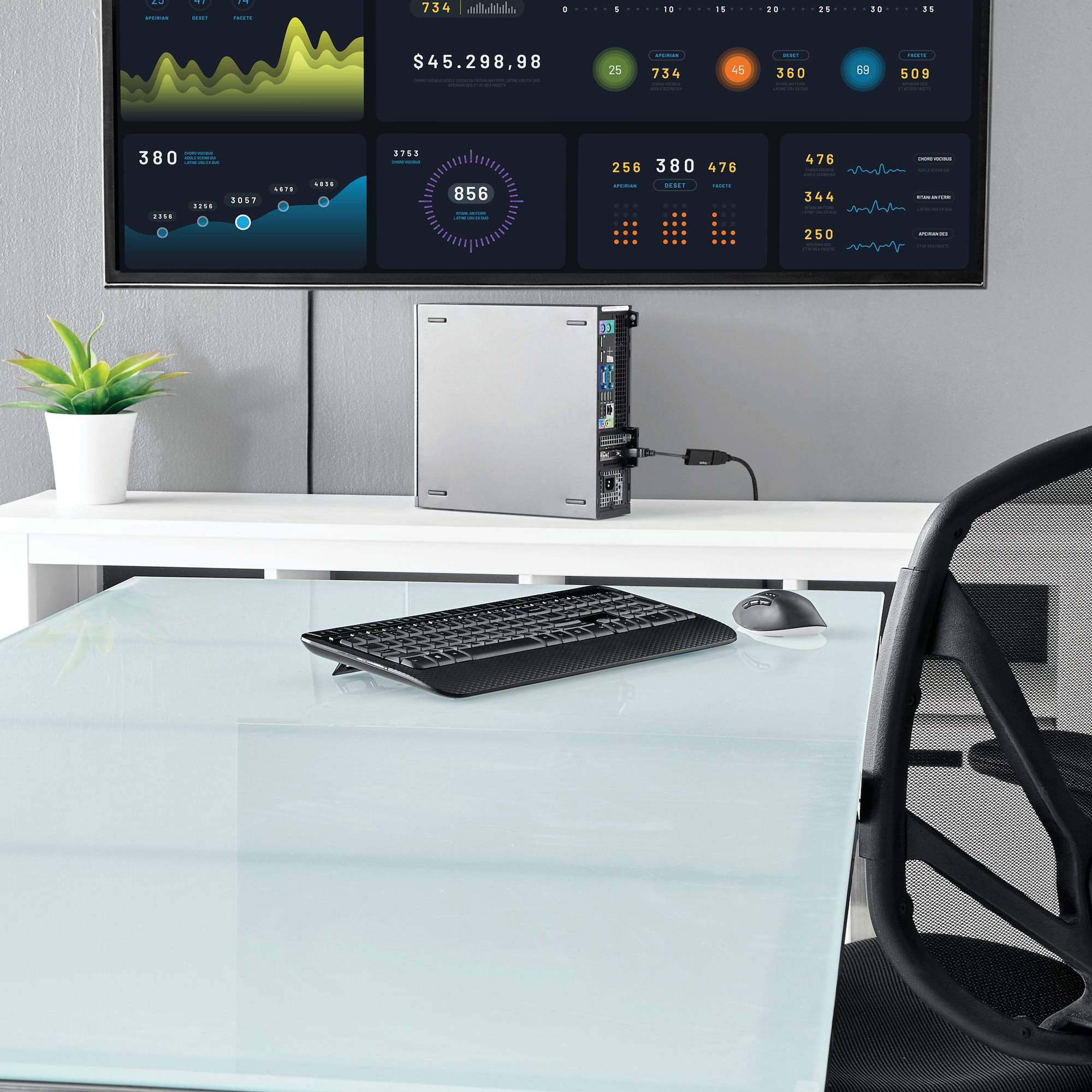Un escritorio con una computadora y un monitor muestra datos. Se ven un teclado, un ratón y una silla.