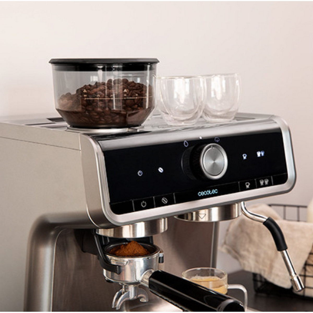 Una macchina da caffè con chicchi di caffè in un contenitore, due bicchieri e un portafiltro con fondi di caffè.