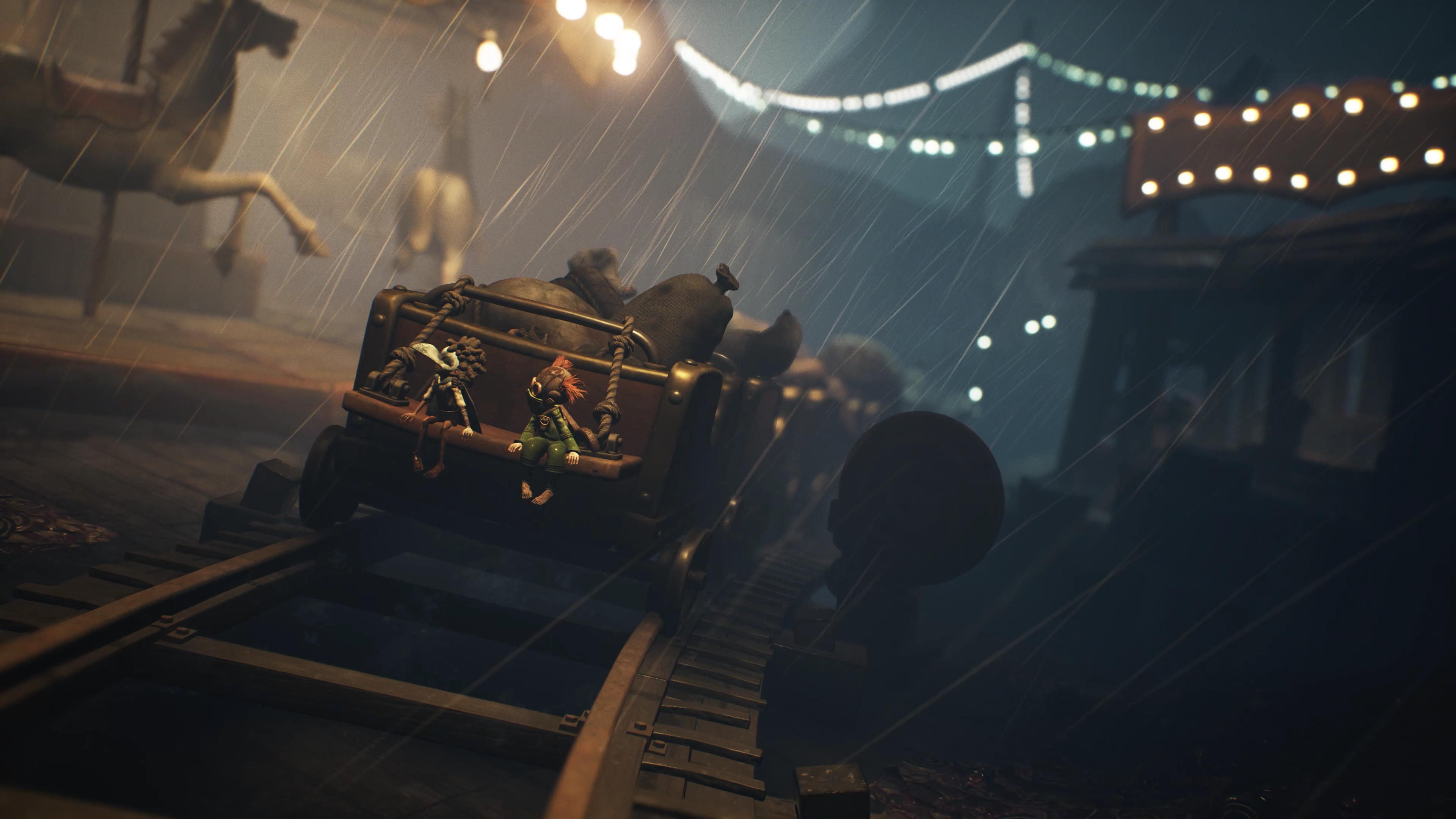 Deszczowa scena w parku rozrywki. Wózek z dwiema postaciami na torach. Karuzela i światła w tle.