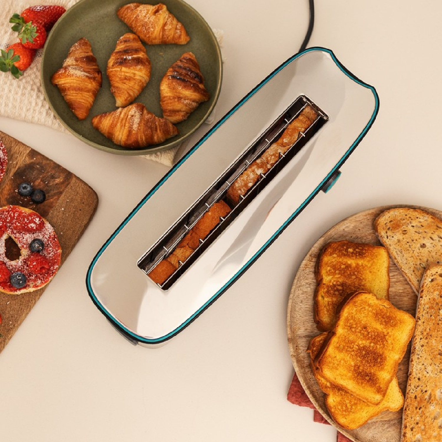 Un tostapane con toast, croissant, fragole e pasticceria. Il cibo è su una superficie bianca con piatti di legno e verdi.